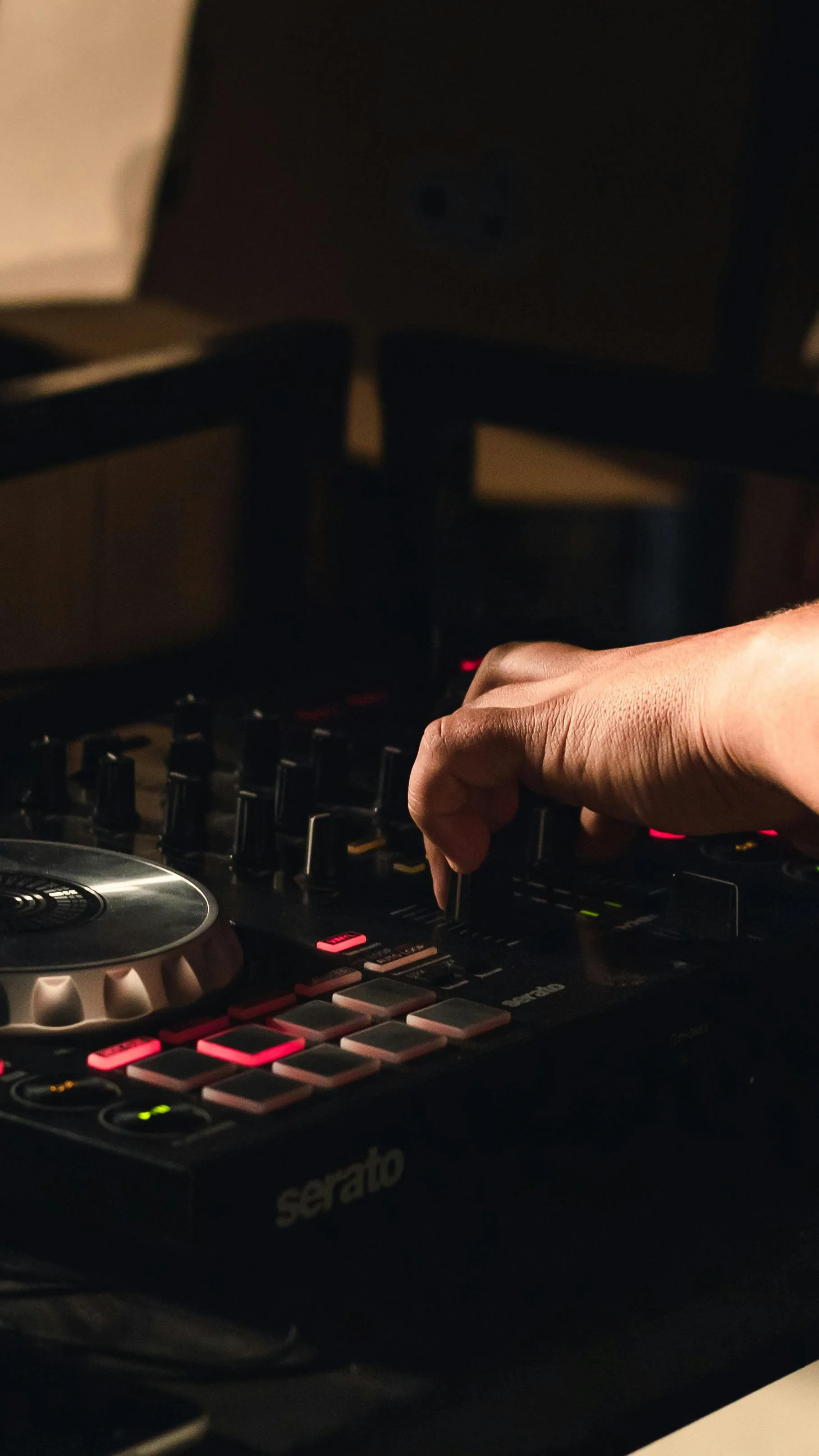 Close-up of a DJ's hand adjusting controls on a DJ controller in a dimly lit setting.