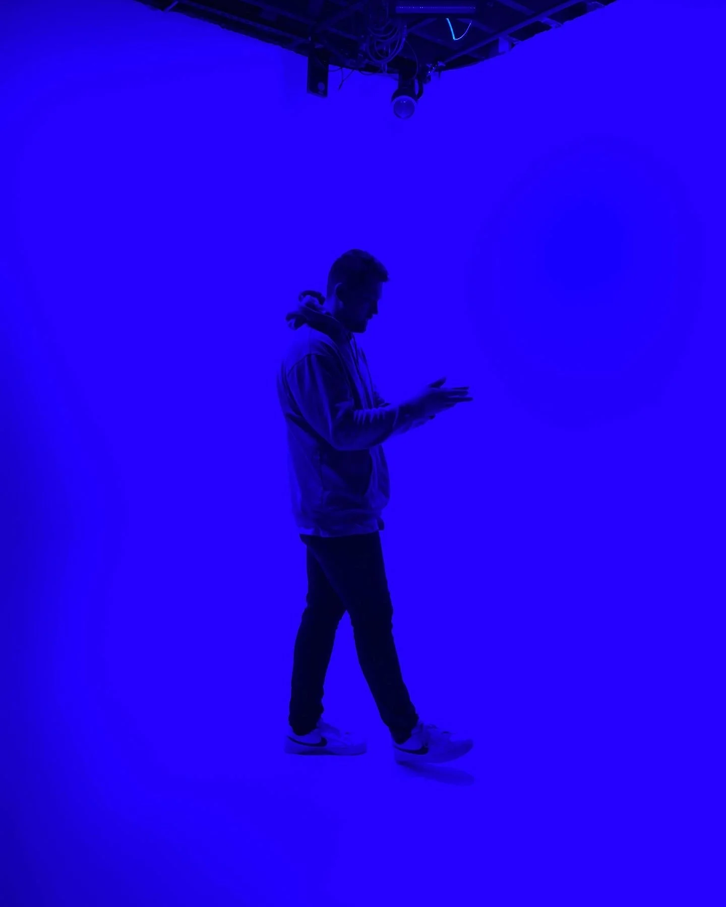 A person standing and looking at their phone in a dark room illuminated by blue light, with equipment hanging from the ceiling.