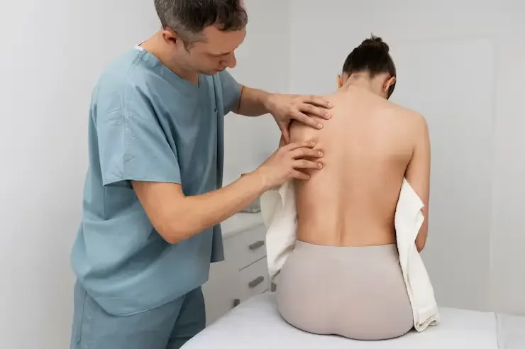 The image depicts a healthcare professional performing a physical examination or massage on the back and shoulder area of a patient.