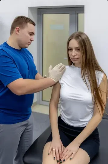 The image shows a healthcare professional performing a physical examination on a female patient's shoulder.