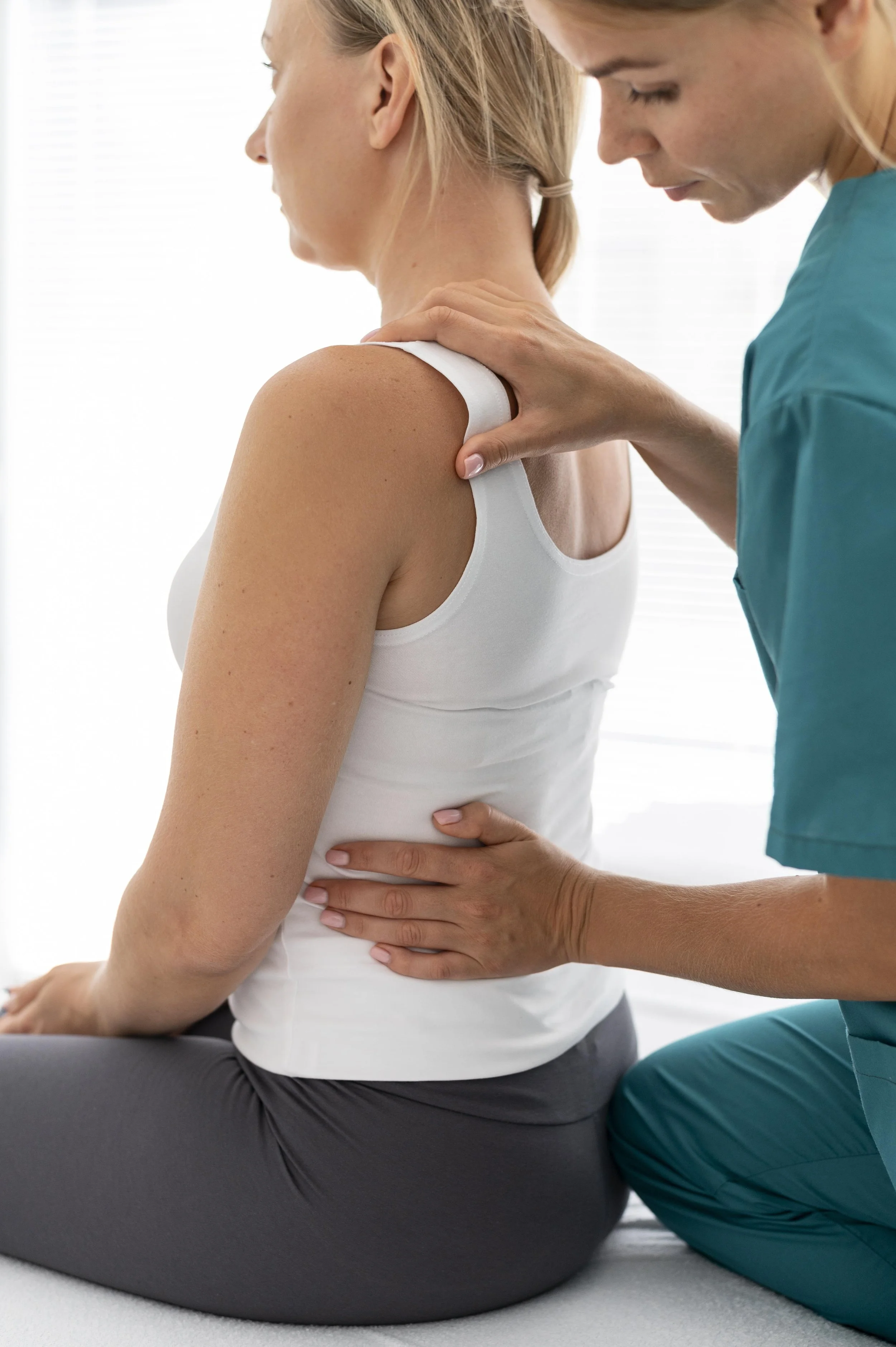 A physical therapist providing manual treatment to a patient's back and shoulder area while she sits on a table.