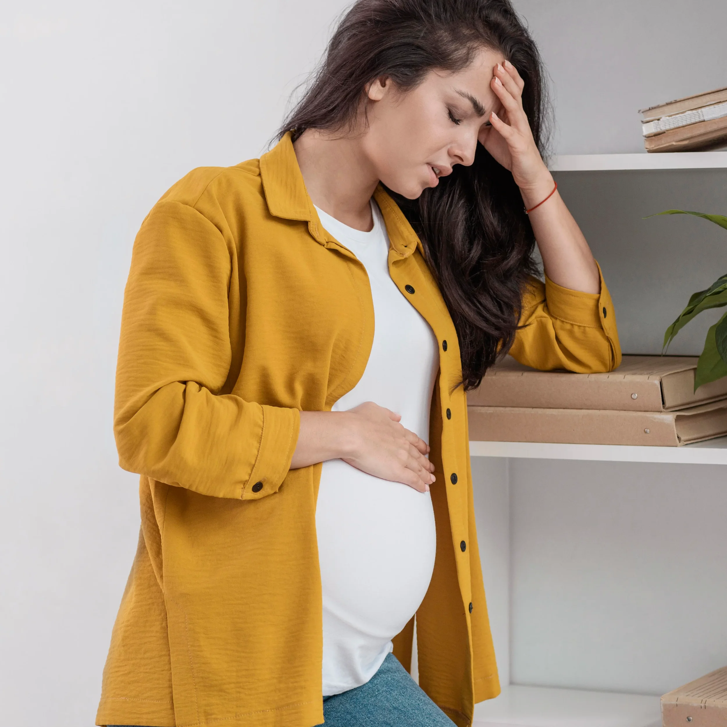 pregnant woman is shown looking distressed while holding her head and stomach.