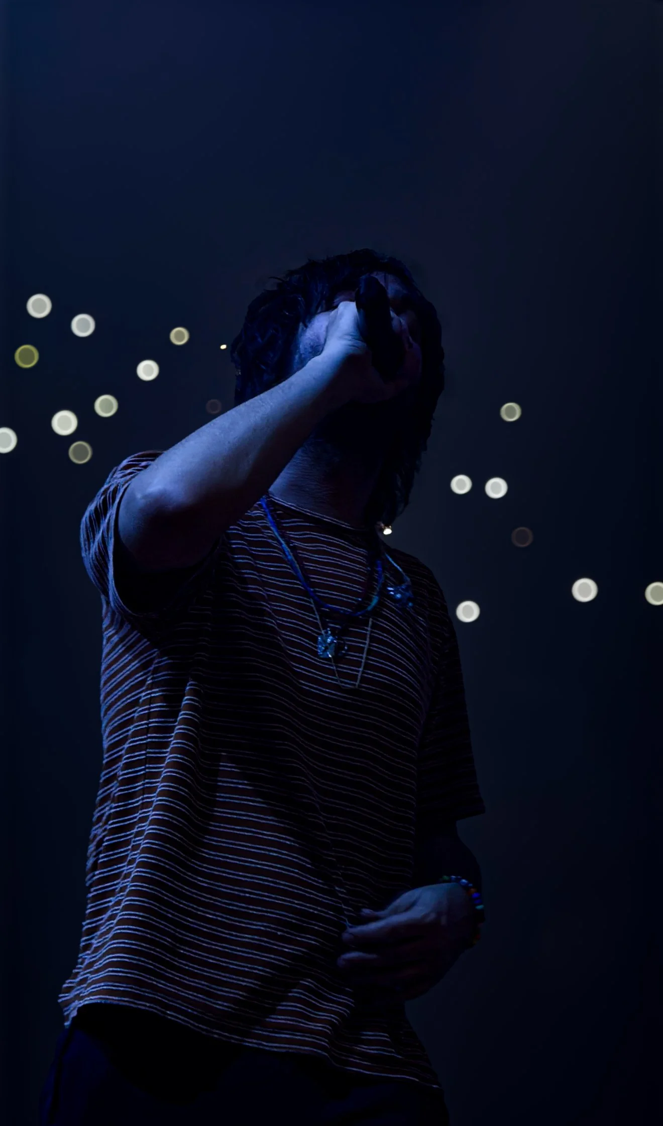 Silhouette of a person singing into a microphone on stage with blurred lights in the background.