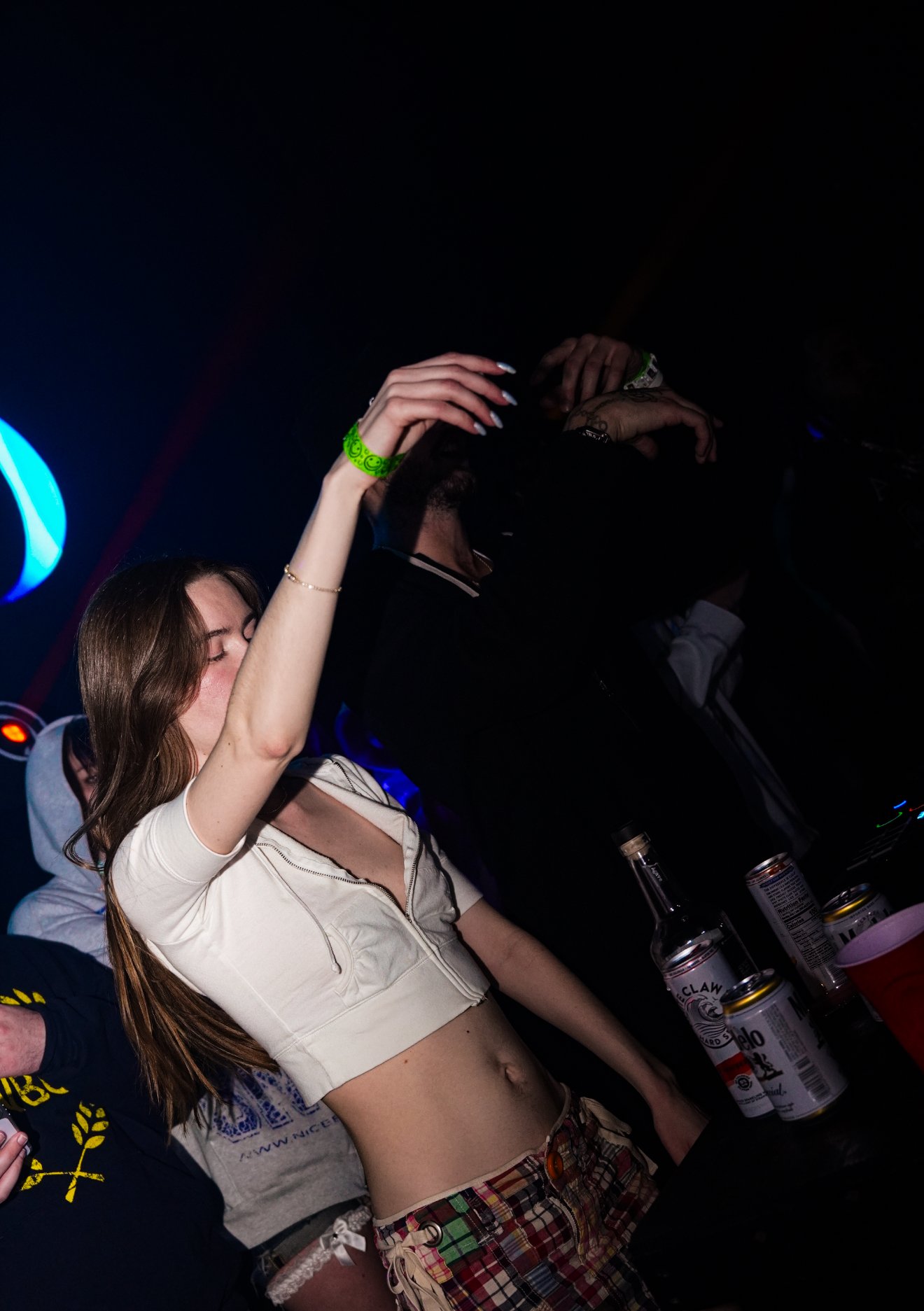 People dancing and having fun at a nightclub with bottles and cans of drinks on the table.