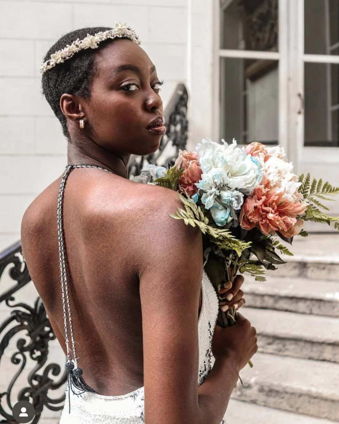 A black bride with a wedding bouquet standing on stairs in Paris. She has a crown on her head.