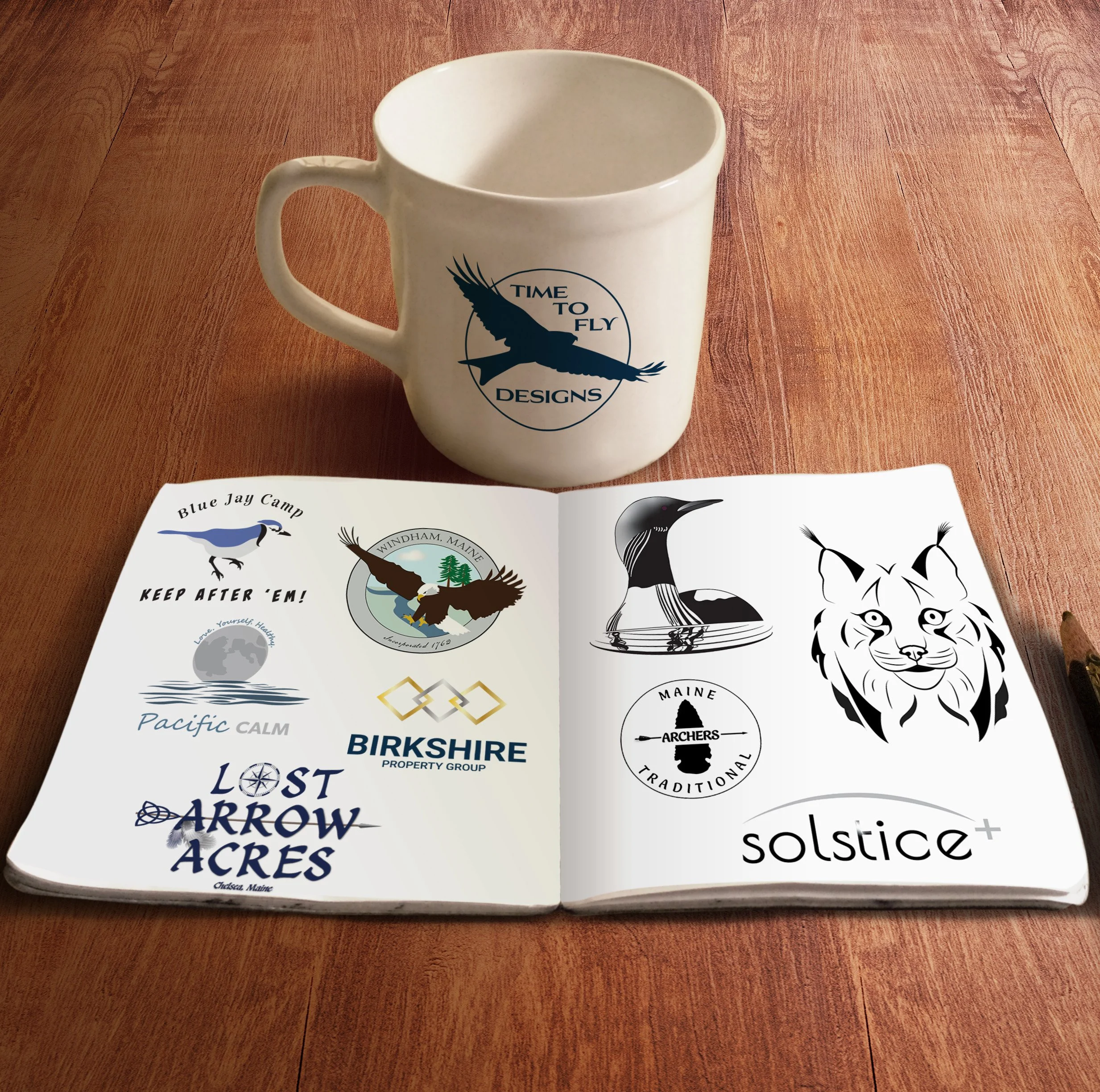 A sketch book with logo designs on a table in front of a coffee cup with the logo for Time To Fly Designs