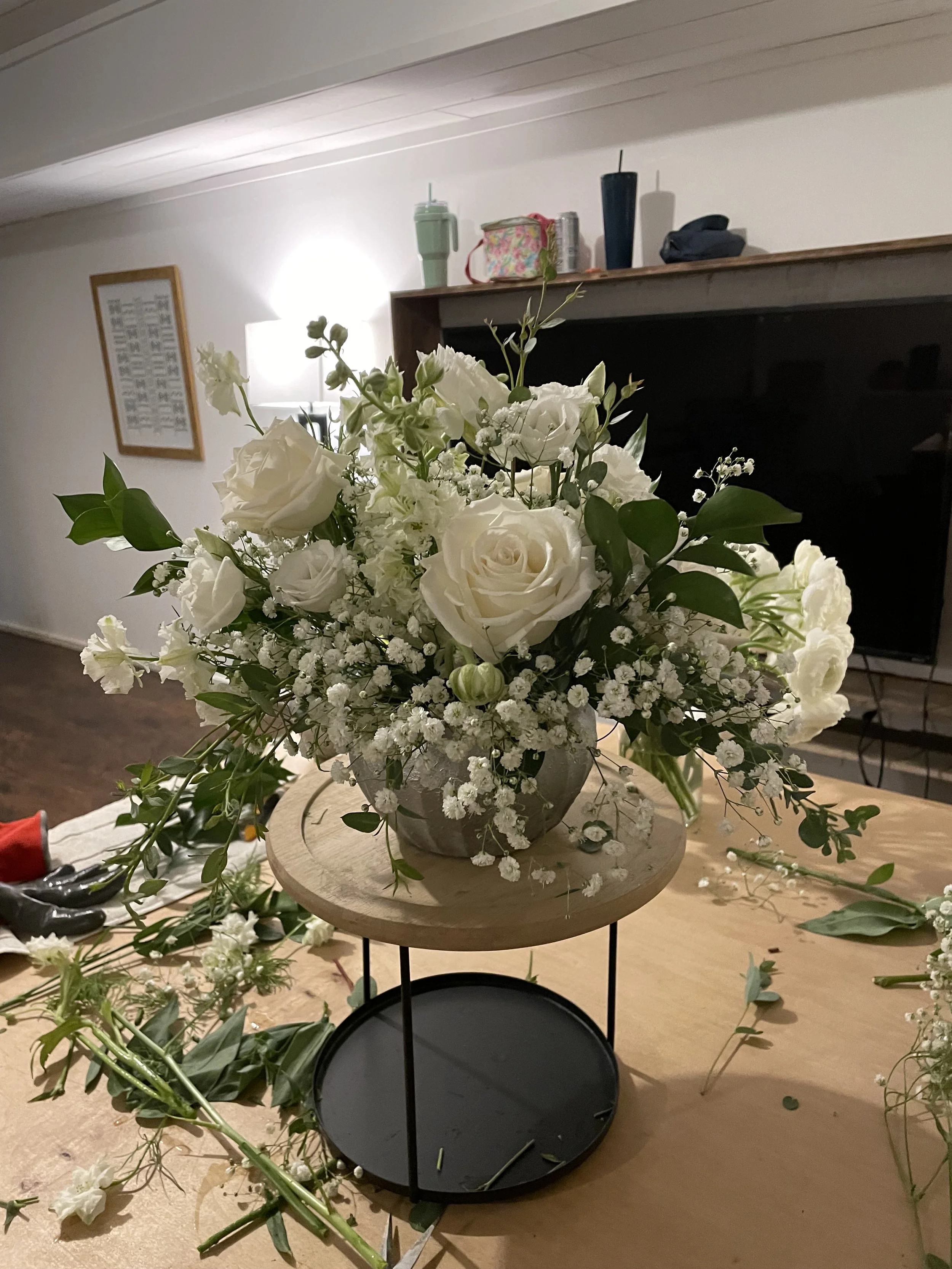 A flower arrangement with white roses and baby's breath on a two-tiered stand in a living room.