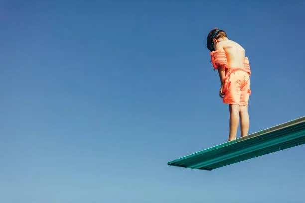 A boy stands on a diving board in armbands, and considers whether to jump