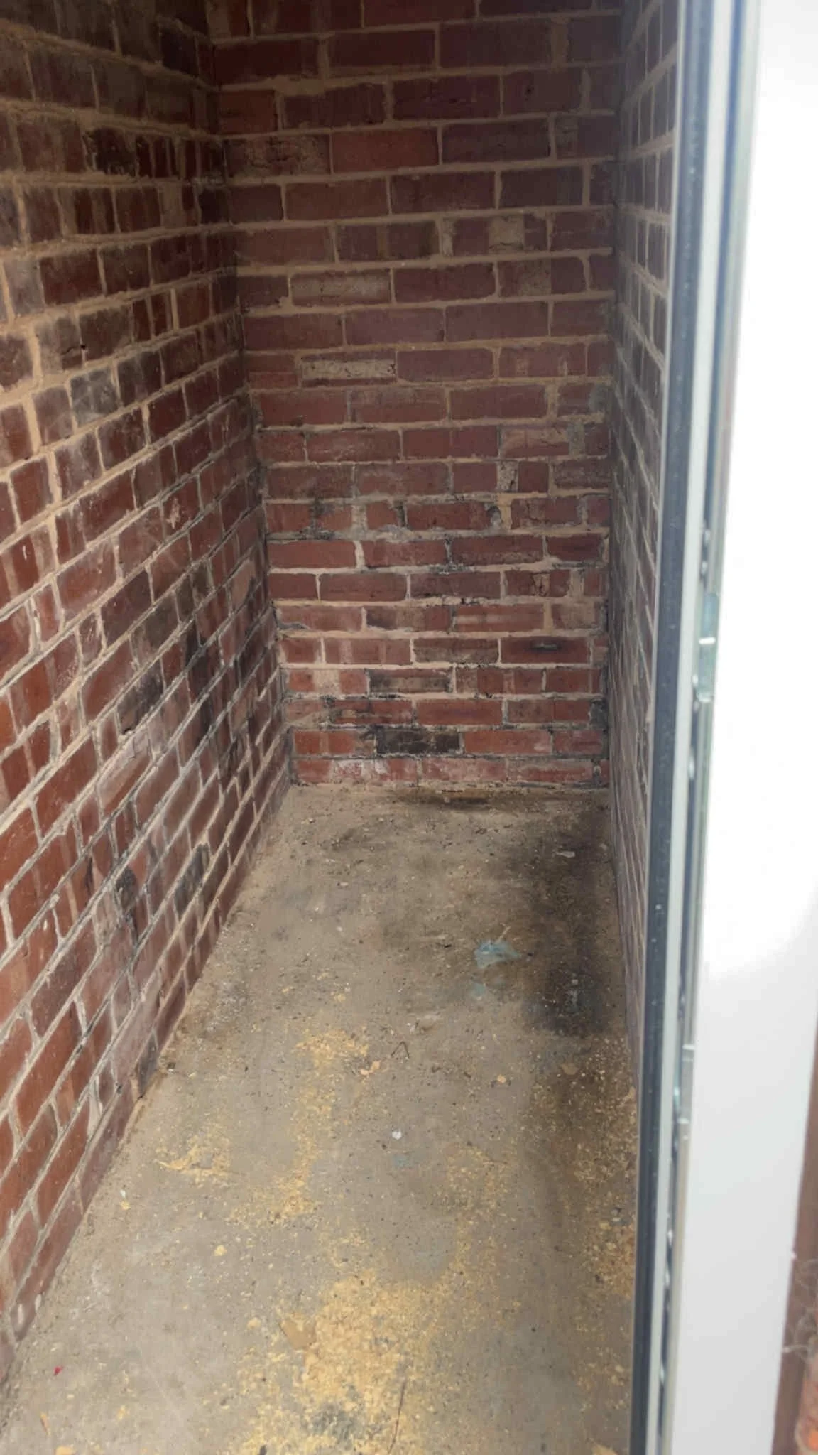 Small enclosed space with red brick walls and a concrete floor, possibly a closet or storage area.