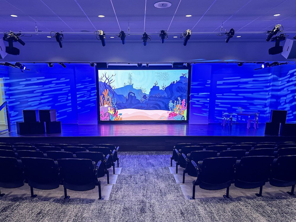 A wide LED screen on a stage, displaying a bright blue and purple animated underwater scene for an event.