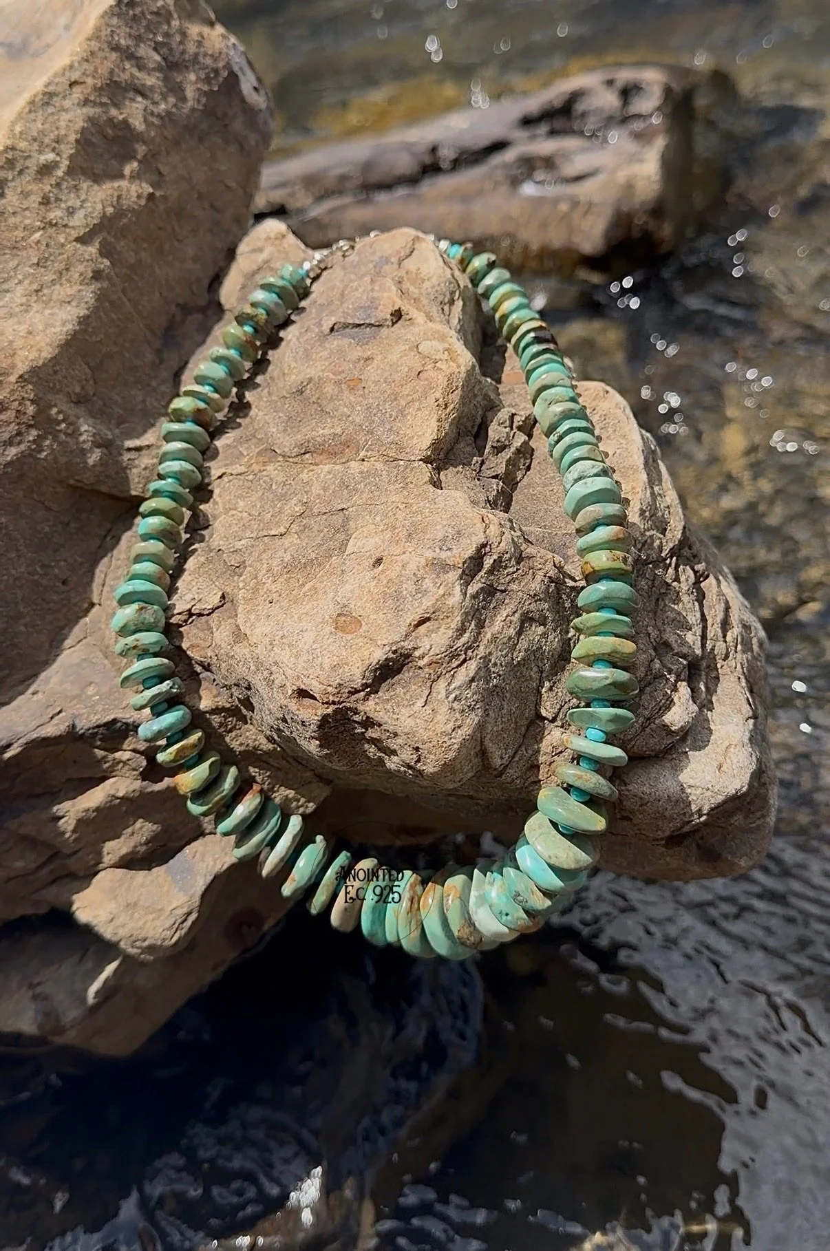 Turquoise shell necklace draped over rocks near water.