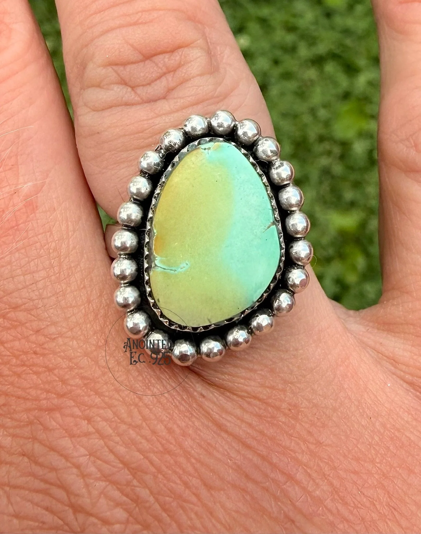 Close-up of a person's finger wearing a large silver ring with an oval-shaped opal gemstone surrounded by small silver beads.