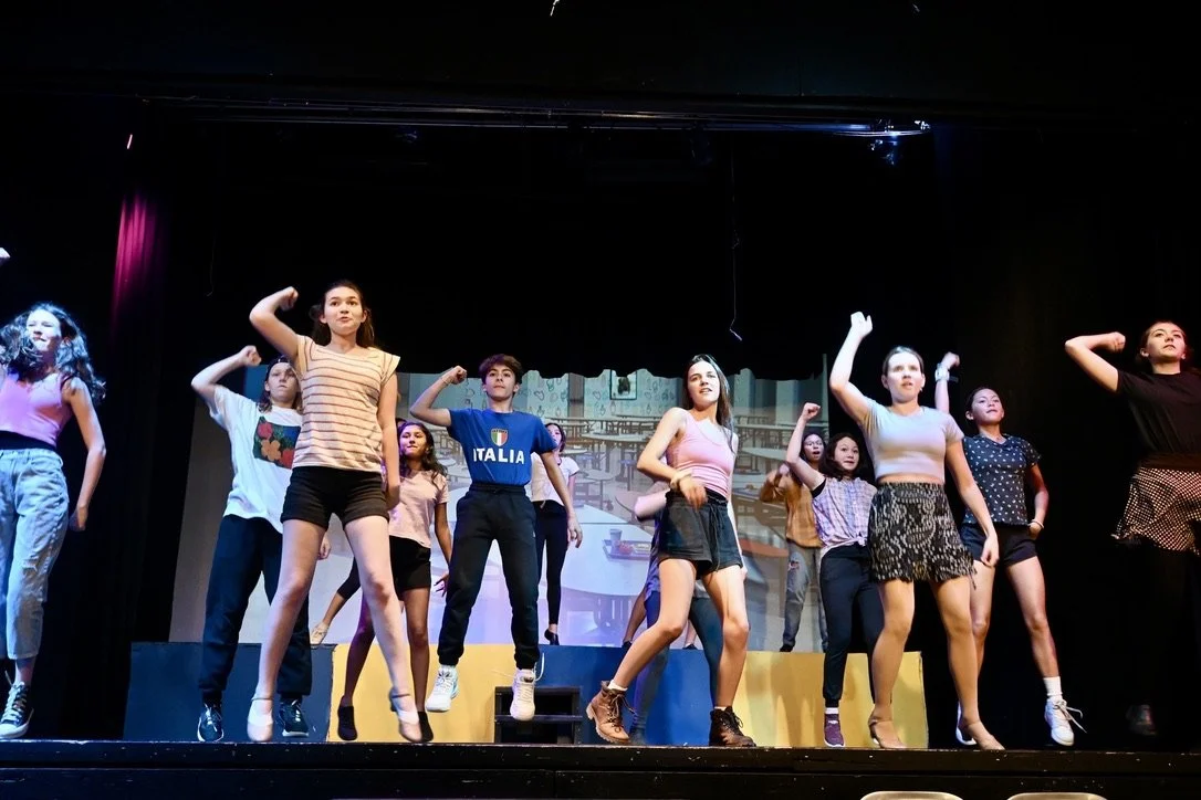A group of young performers on stage during a dance performance, some with their fists raised in a choreographed pose.