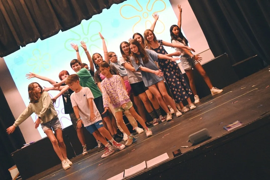 Group of children and teenagers performing on stage with a colorful backdrop of flowers.