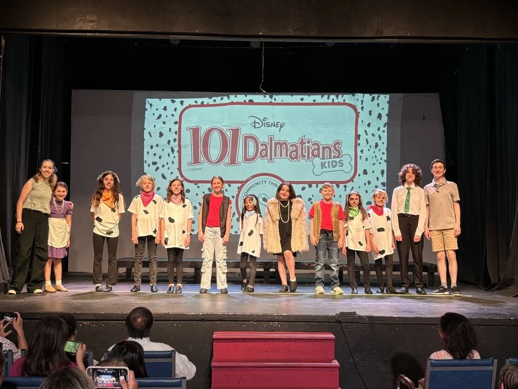 Children and youth on stage performing or presenting for '101 Dalmatians Kids' in a theater or auditorium setting.