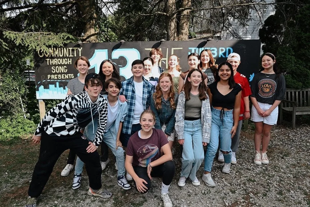 Group of young teenagers standing outdoors in front of a blackboard with graffiti art and text, smiling at the camera.
