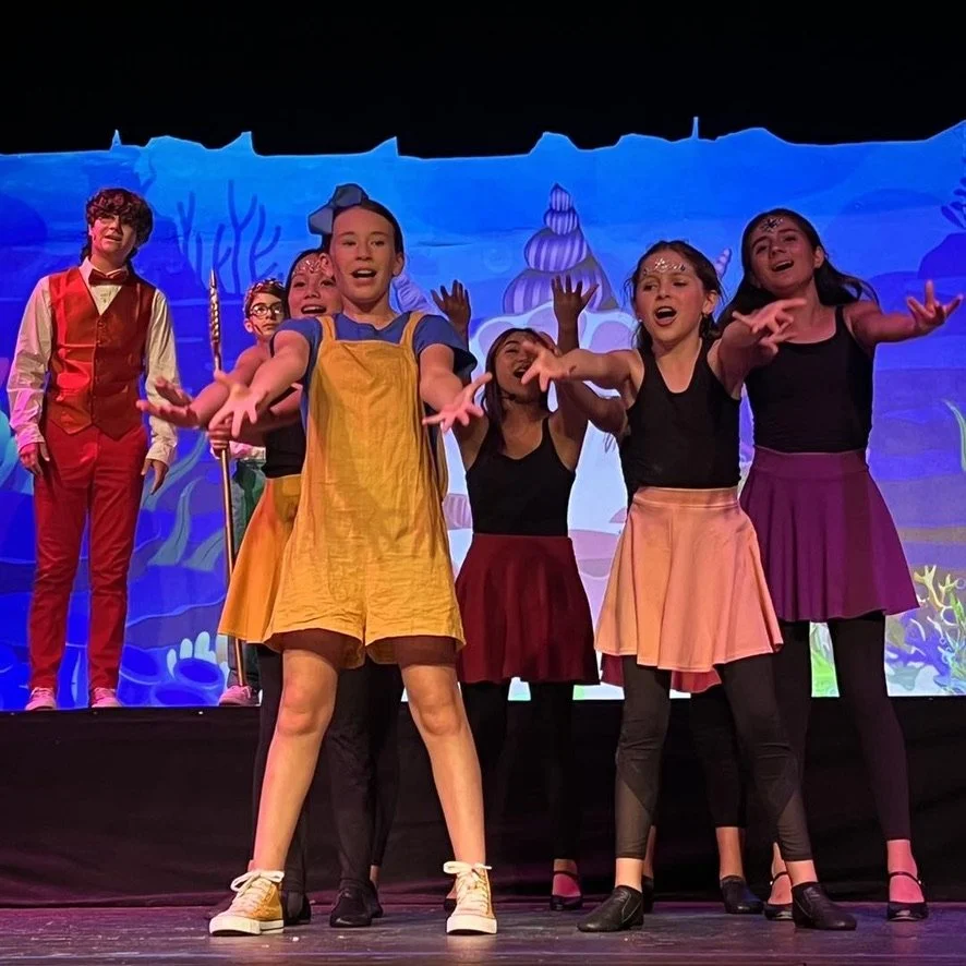 Children performing on stage in colorful costumes, with a backdrop of an animated ocean scene.