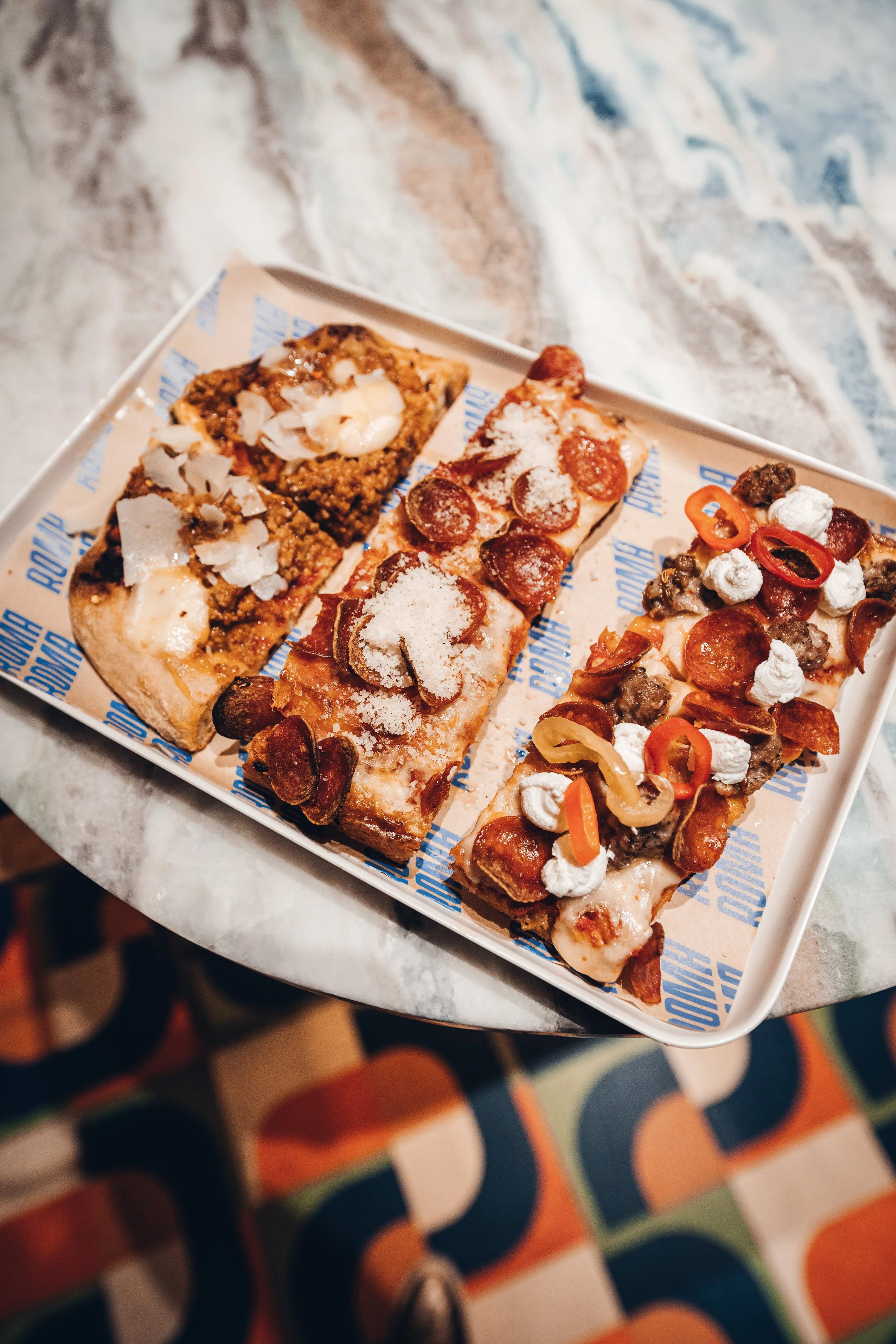 A white tray containing three slices of pizza with various toppings, sitting on a marble table.