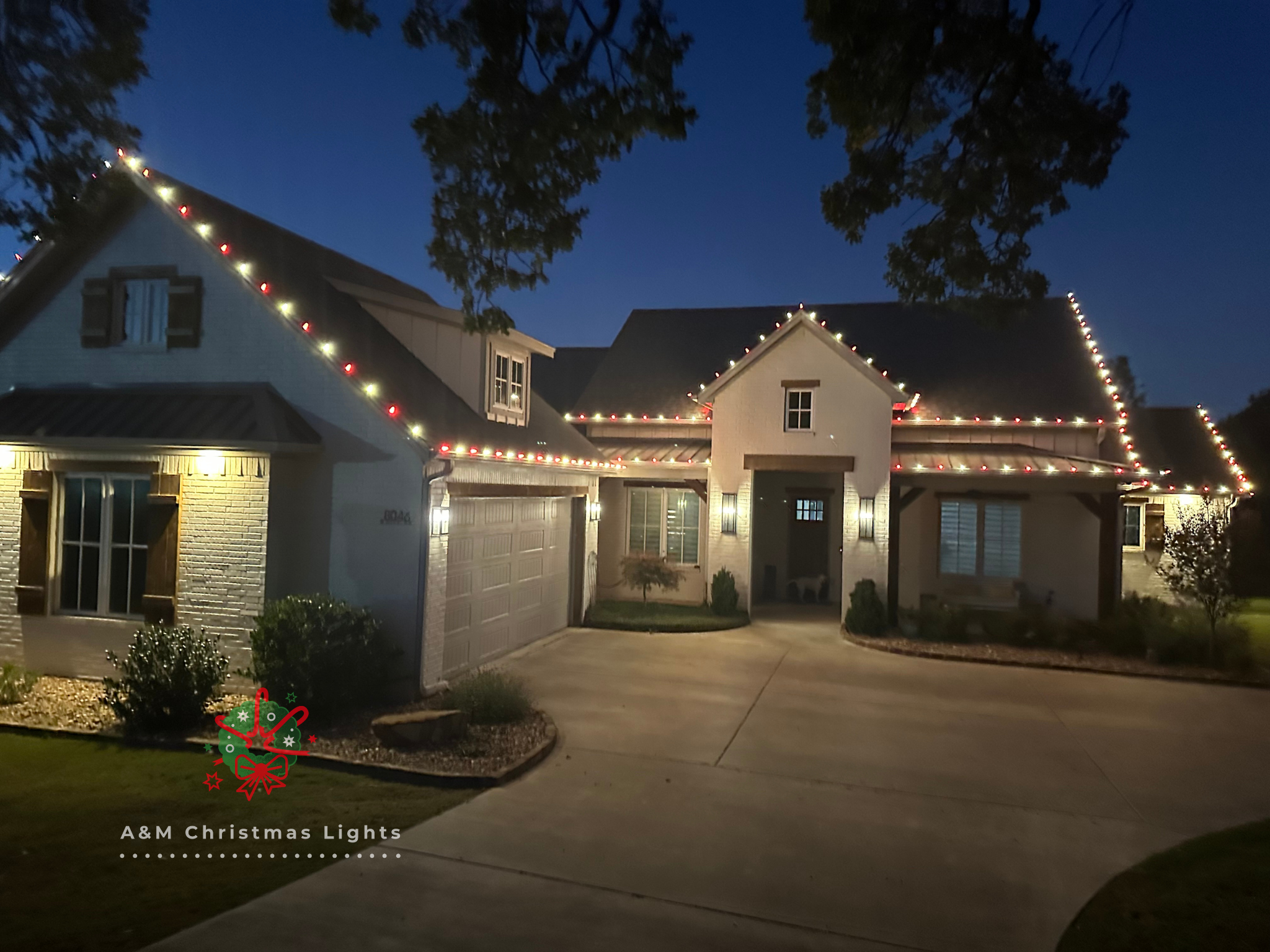 A house decorated with Christmas lights outlining the roof, with a lawn and driveway in the foreground at dusk.