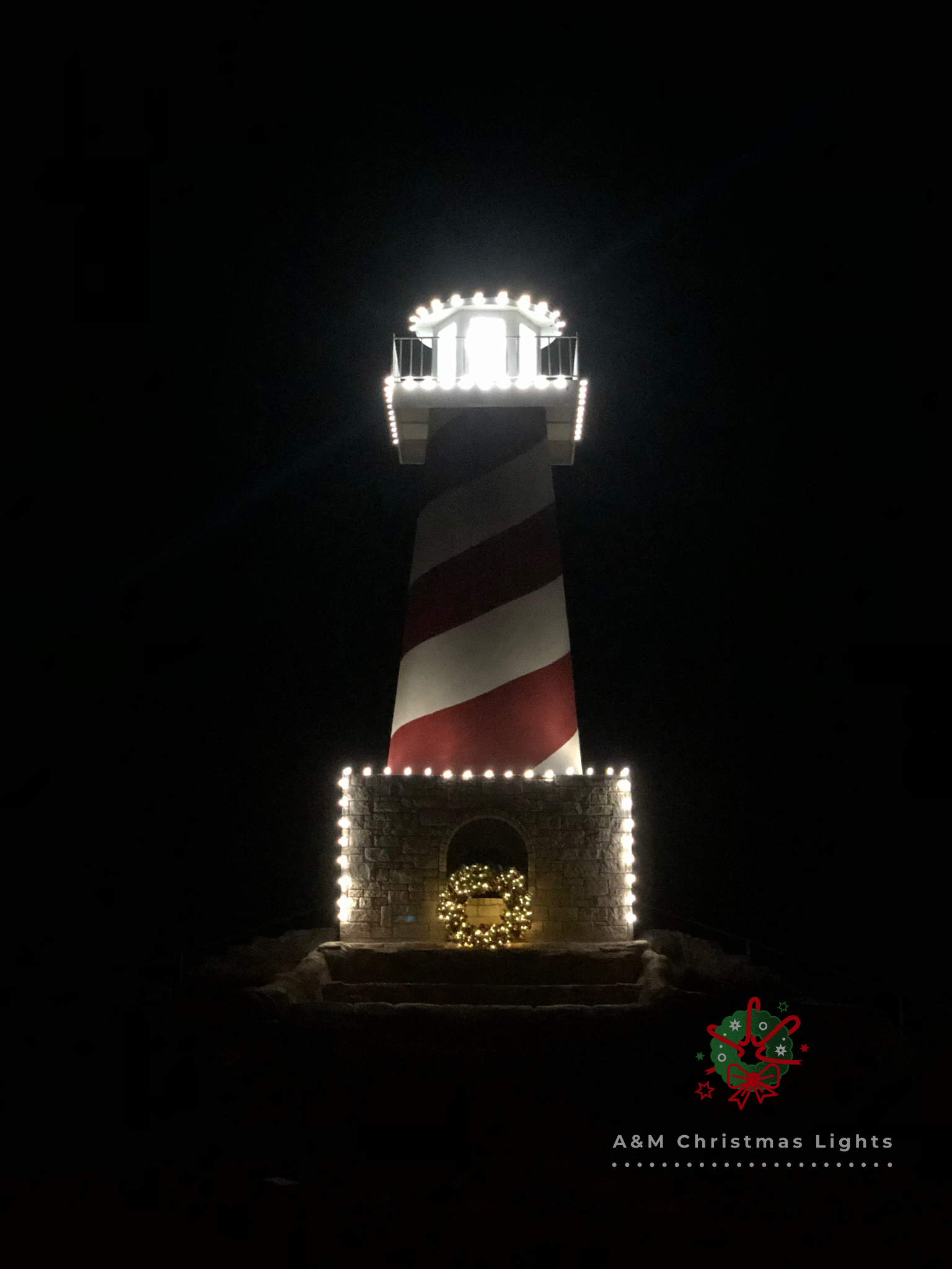 Night view of a lighthouse decorated with Christmas lights, a wreath, and a Christmas gift box at the base, with the text 'A & M Christmas Lights' and a festive decoration.
