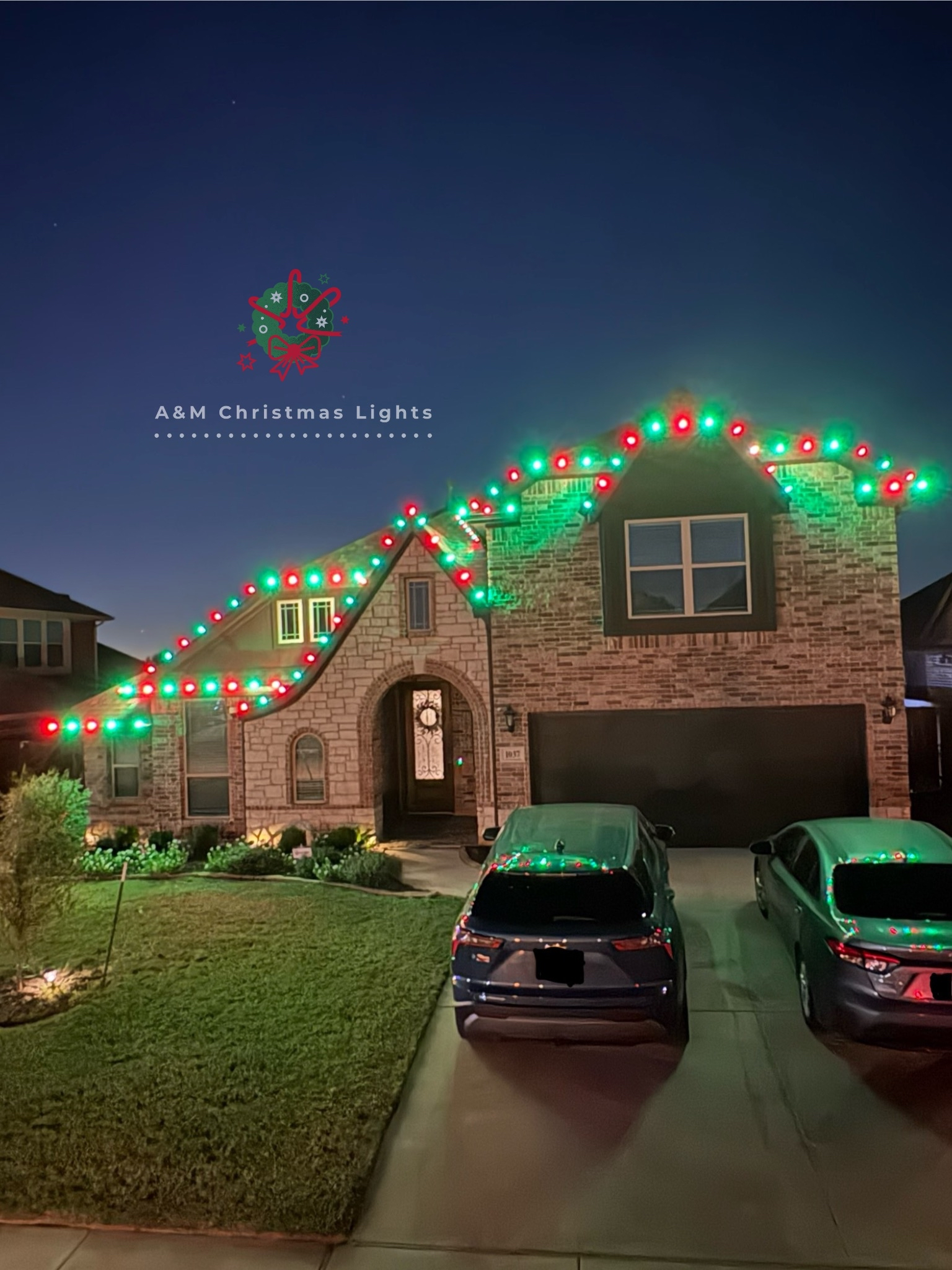 A house decorated with red and green Christmas lights along the roofline at dusk. The front yard has a lawn and garden. Two cars are parked in the driveway. There is a logo with holiday-themed design and text overlay that reads 'A&M Christmas Lights.