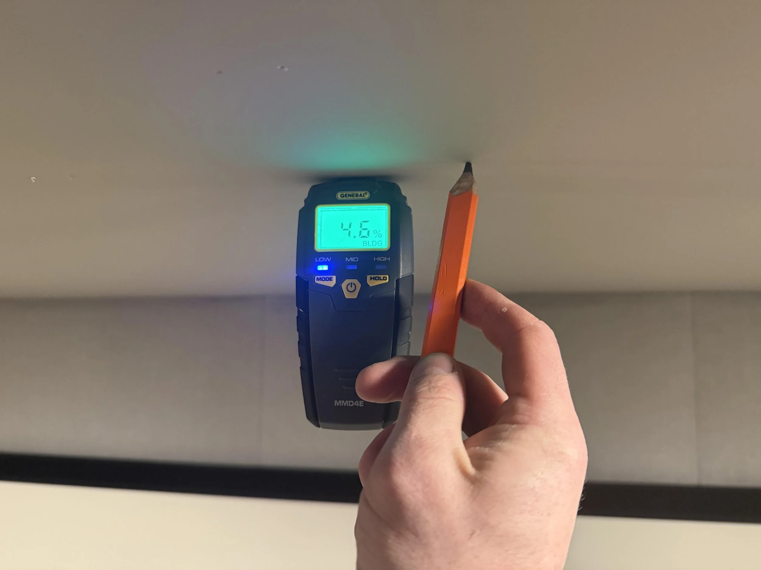 A person measuring moisture level in ceiling drywall with a moisture meter, reading 4.6%.
