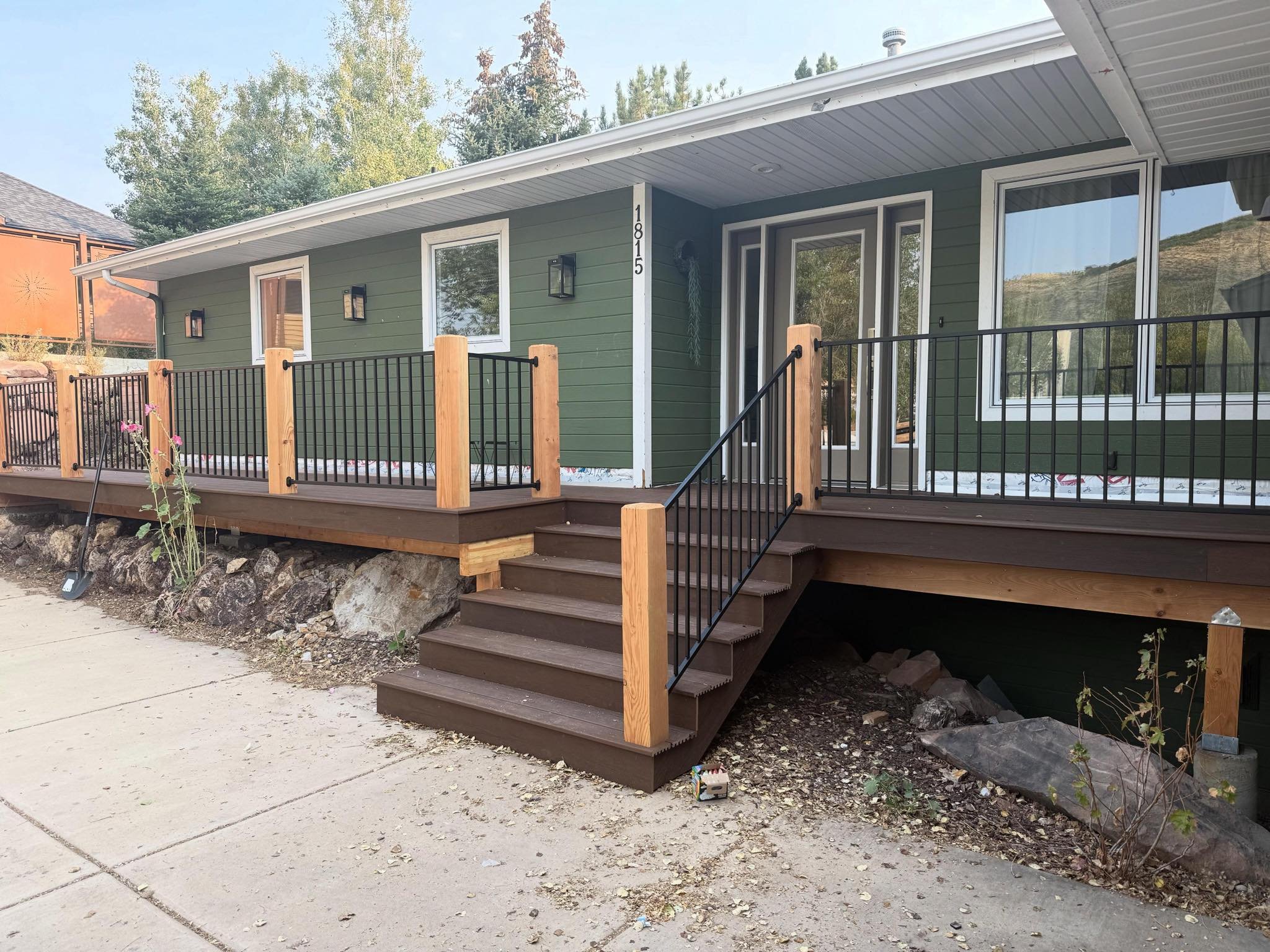 Newly constructed wooden and metal staircase leading to a green house with a deck, glass sliding door, and large front windows.