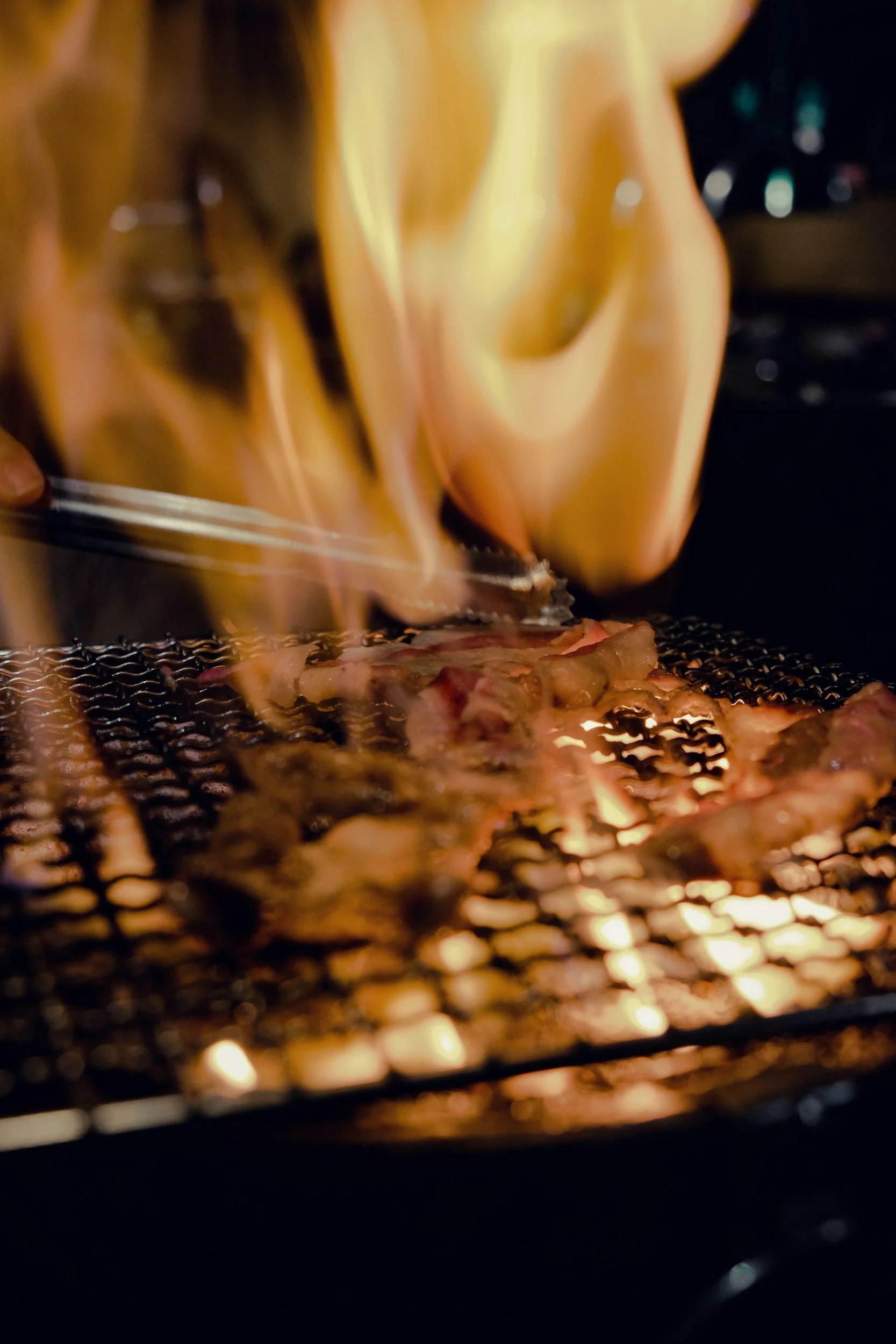 Meat being grilled on a barbecue with flames.