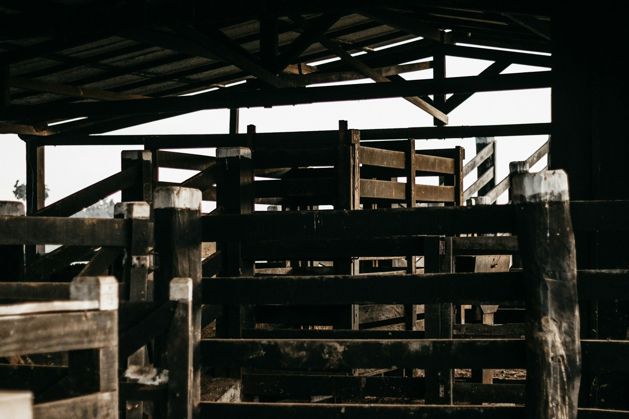 Multiple dark wooden chairs and tables stacked together inside a rustic wooden structure.