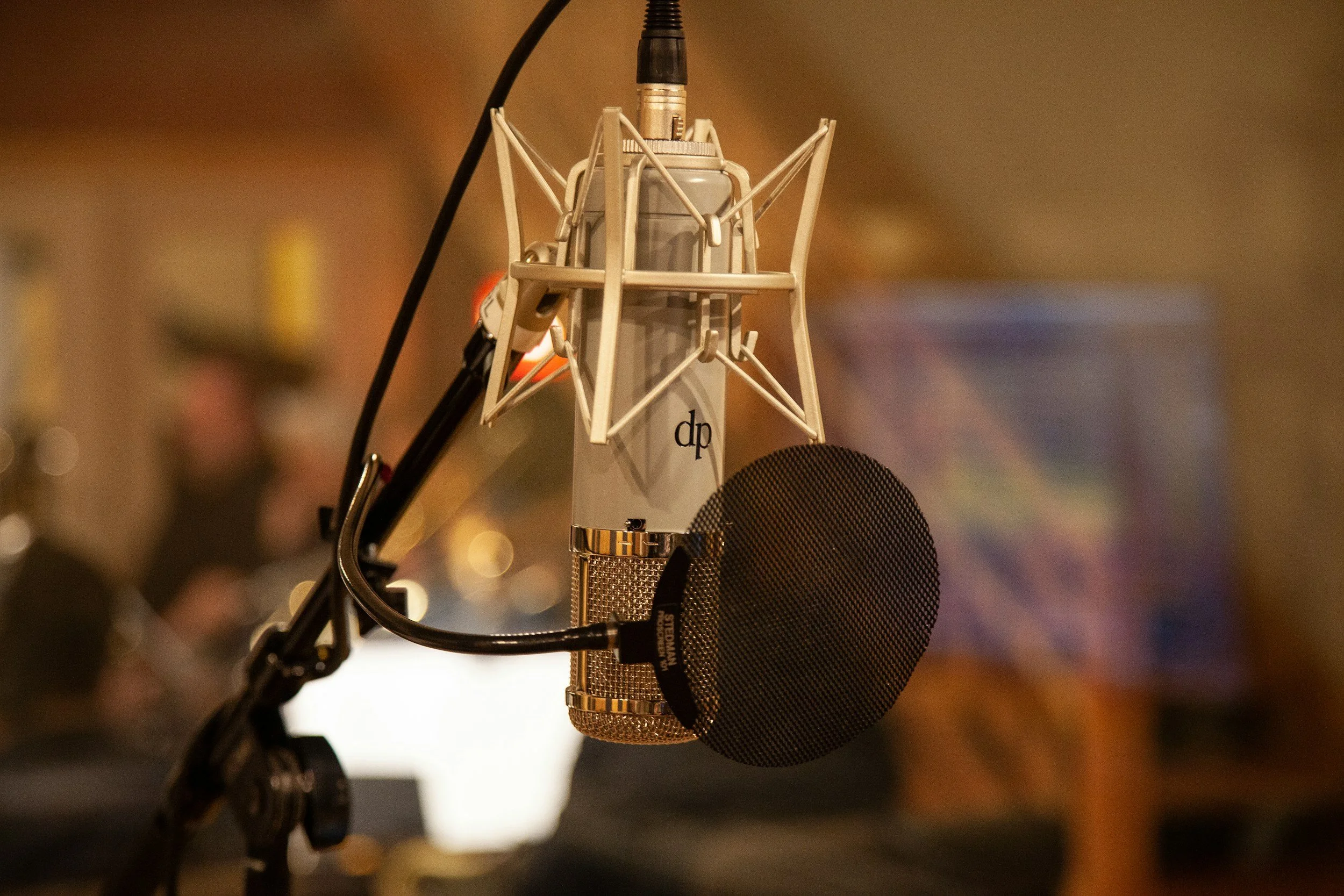 A professional recording microphone with a pop filter in front and a shock mount, set up in a studio environment.