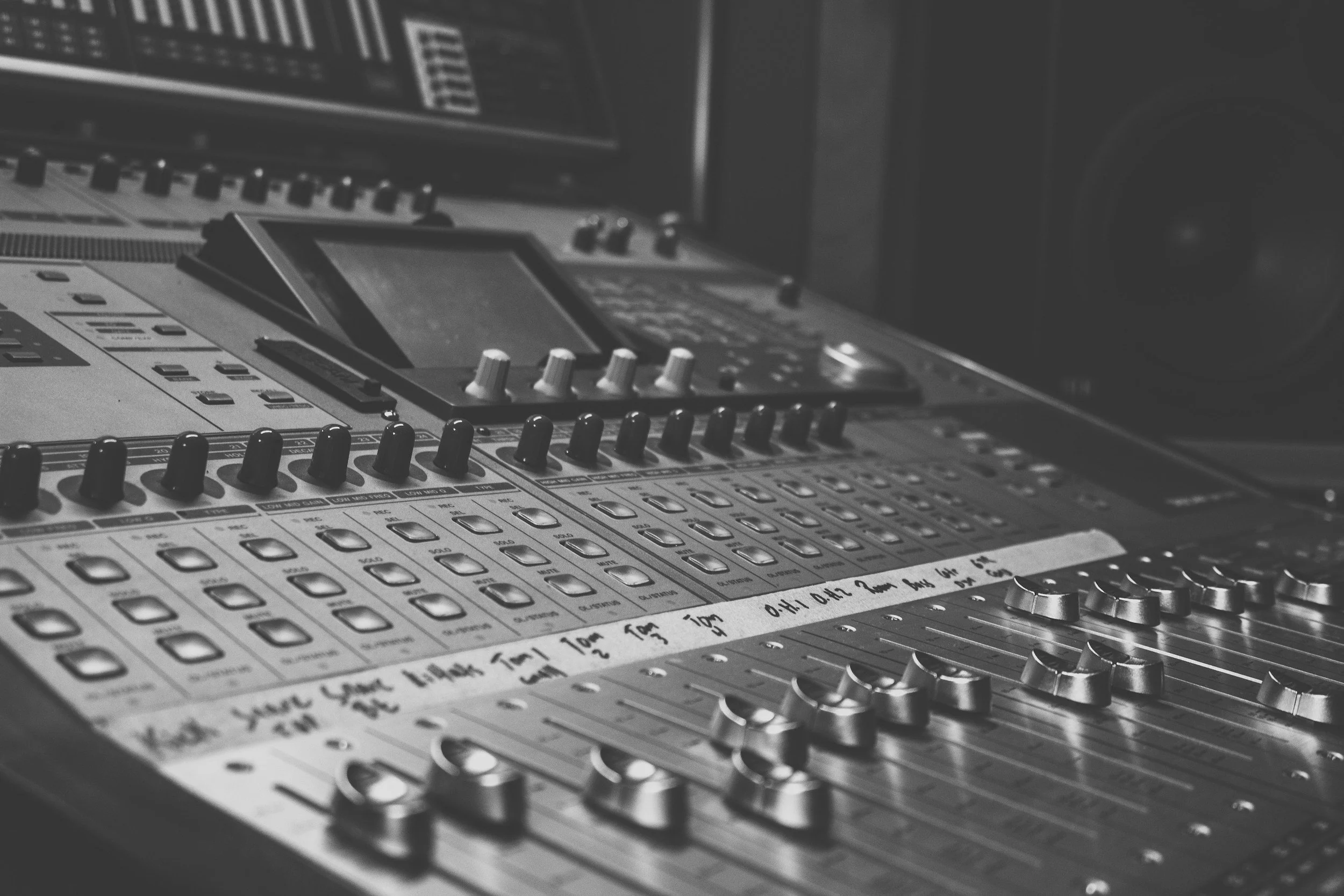 Close-up of a professional audio mixing console with various knobs, faders, and buttons in a recording studio.