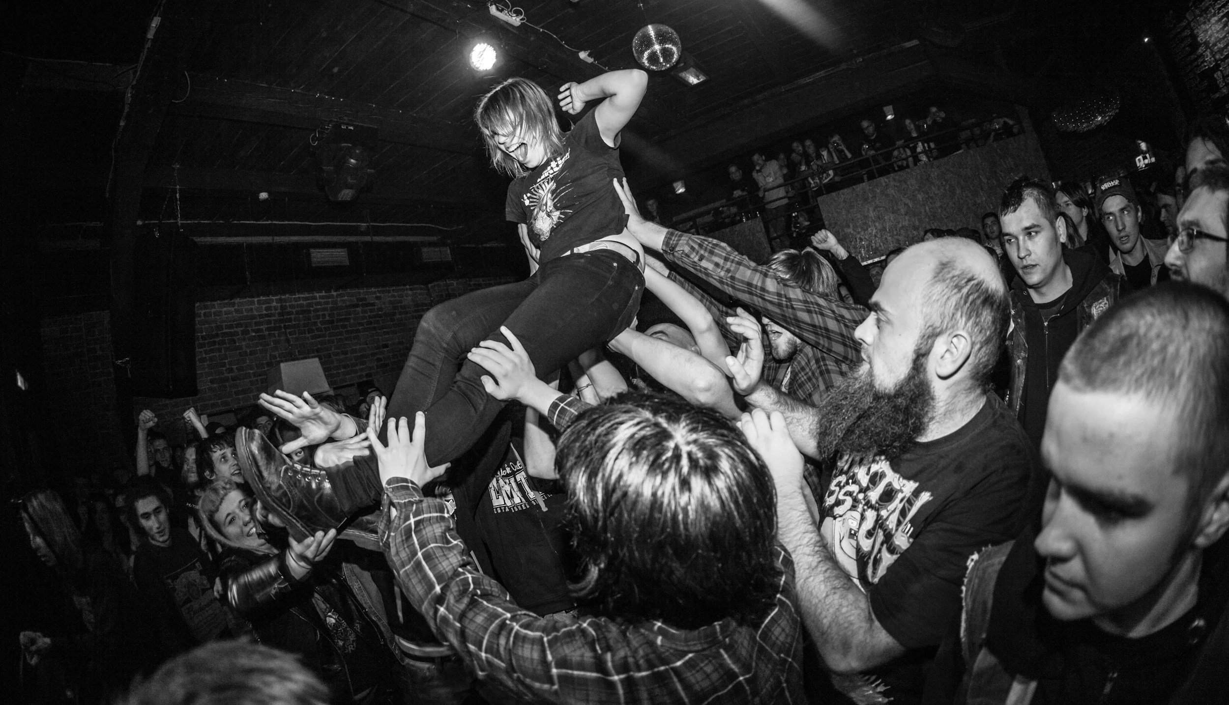 A crowd at a concert lifting a young woman during a mosh pit or crowd surfing.