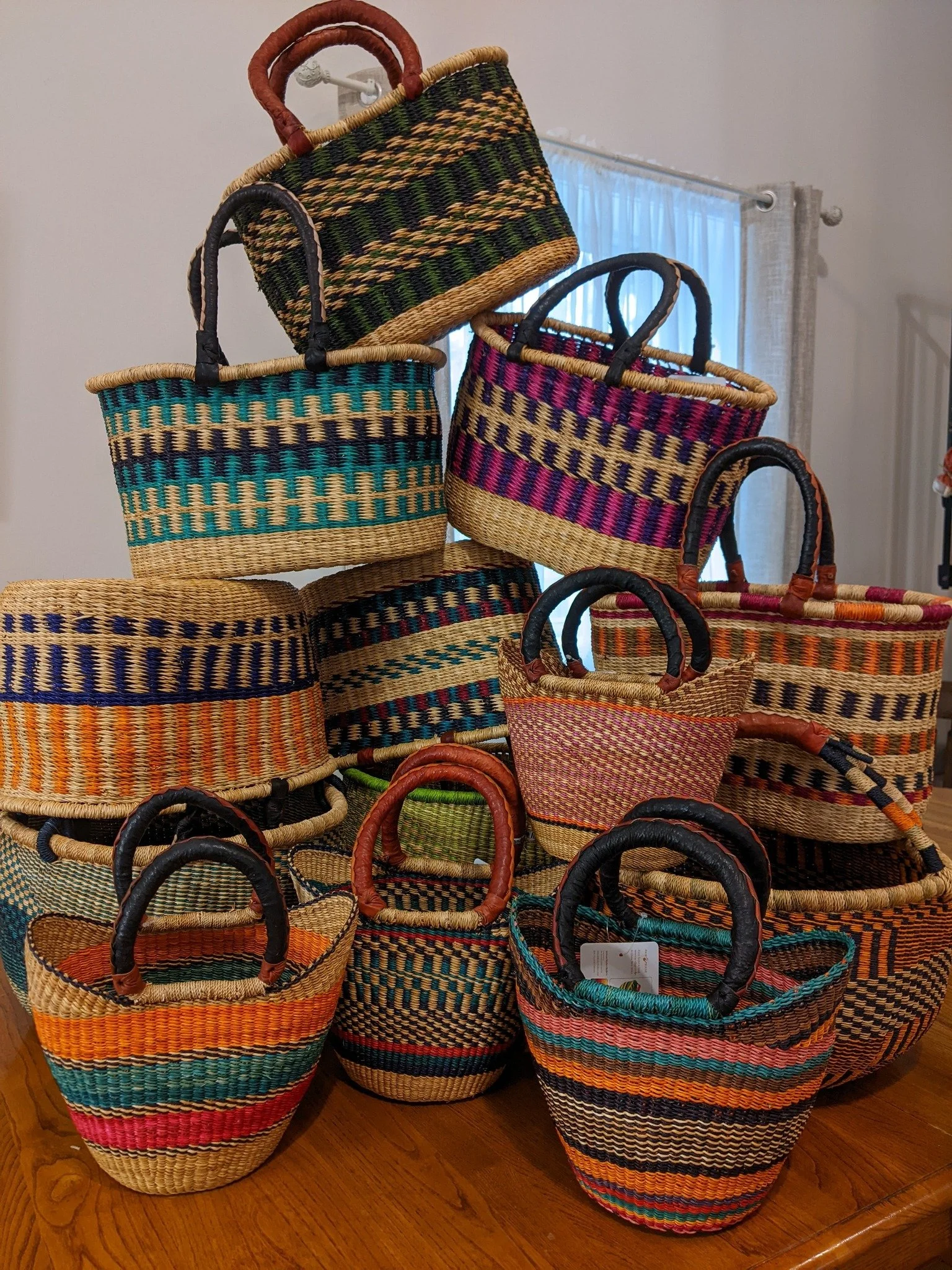 Colorful woven baskets of various sizes and patterns stacked on a wooden surface indoors.