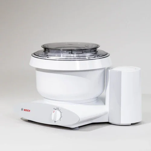 A Bosch stand mixer with a white body, a rotating bowl, and a transparent lid.