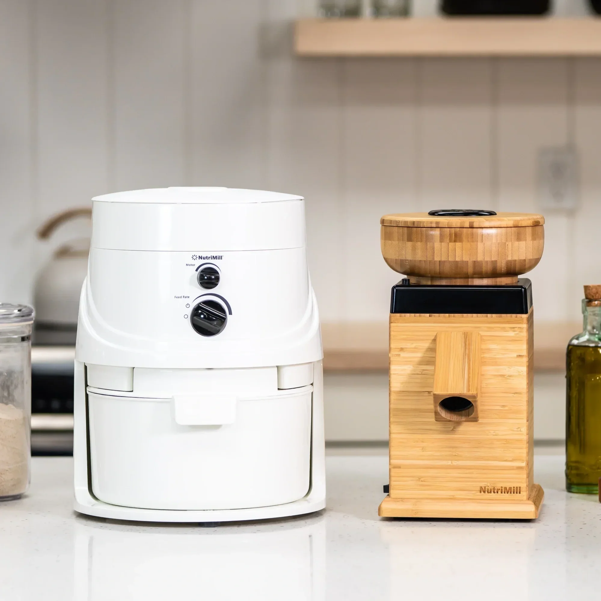 A white NutriMill grain mill and a wooden coffee grinder on a kitchen countertop.