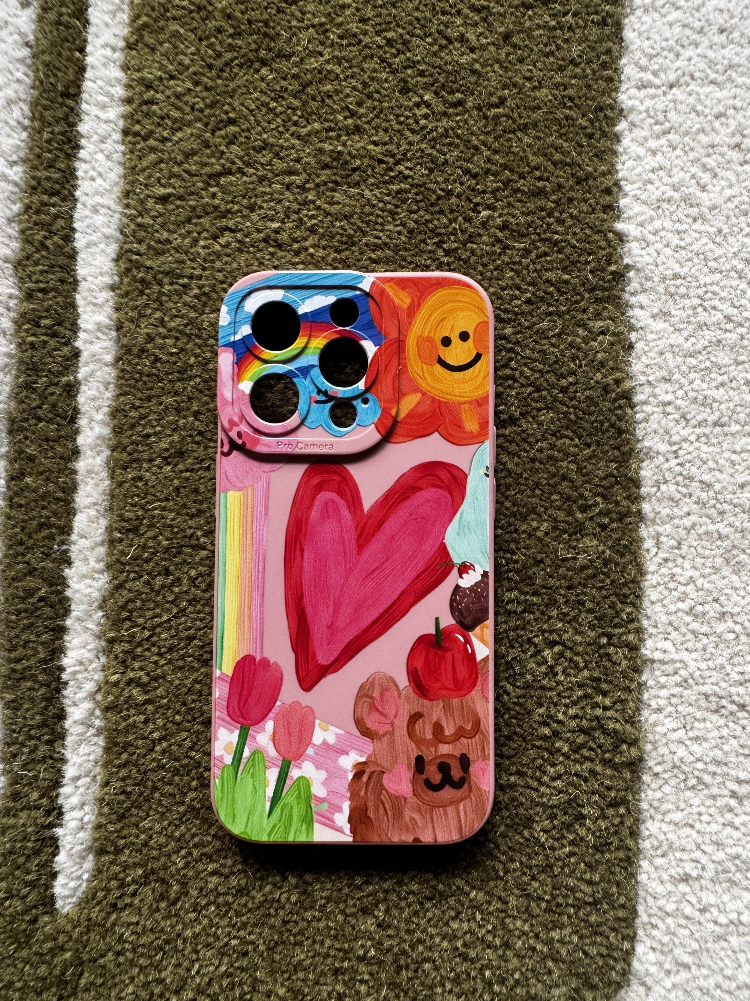 Colorful phone case with hand-drawn illustrations of a lion, hearts, flowers, a dog, and cherries, placed on a striped and textured carpet.
