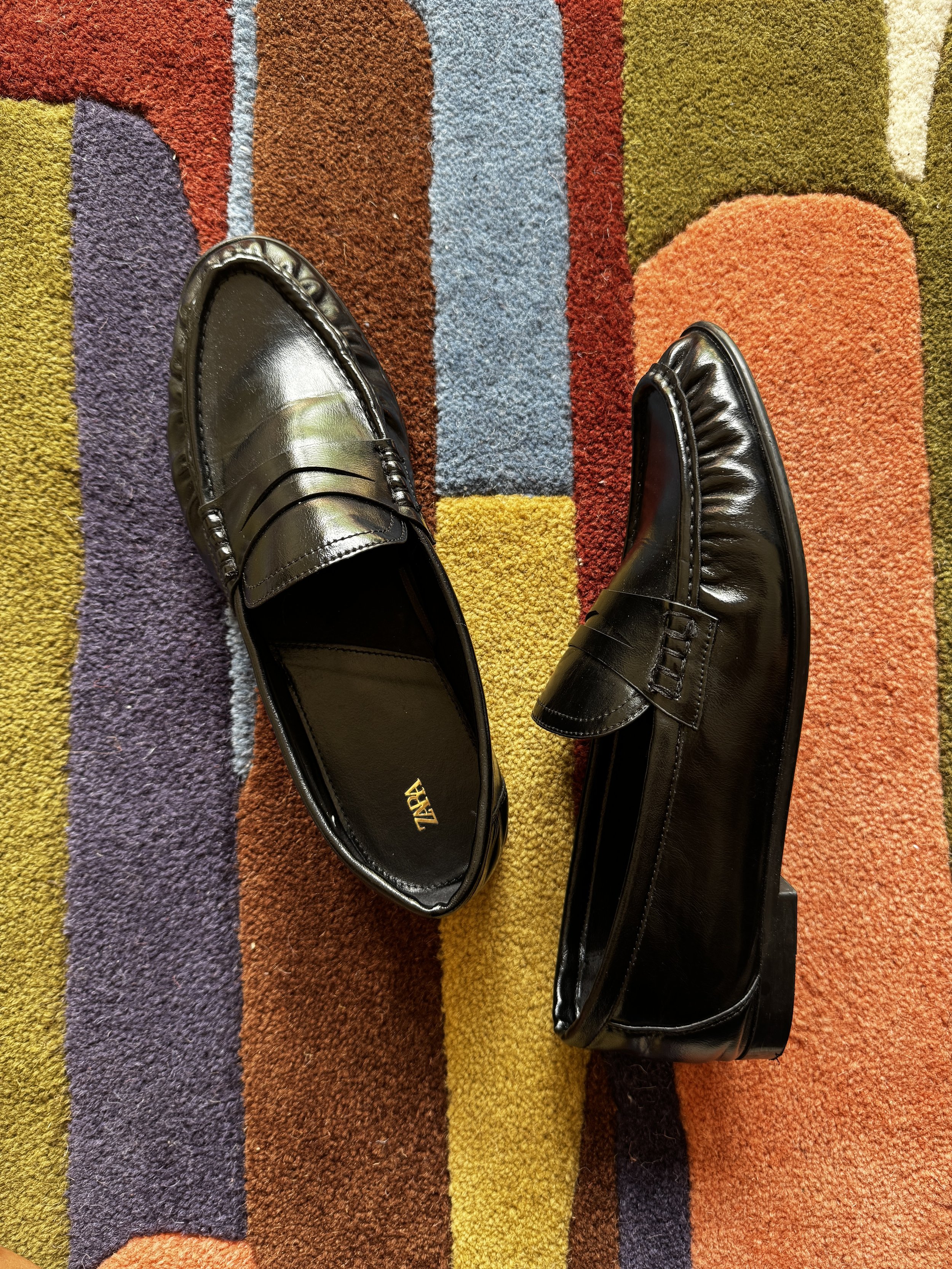 A pair of black leather shoes placed on a colorful striped carpet.