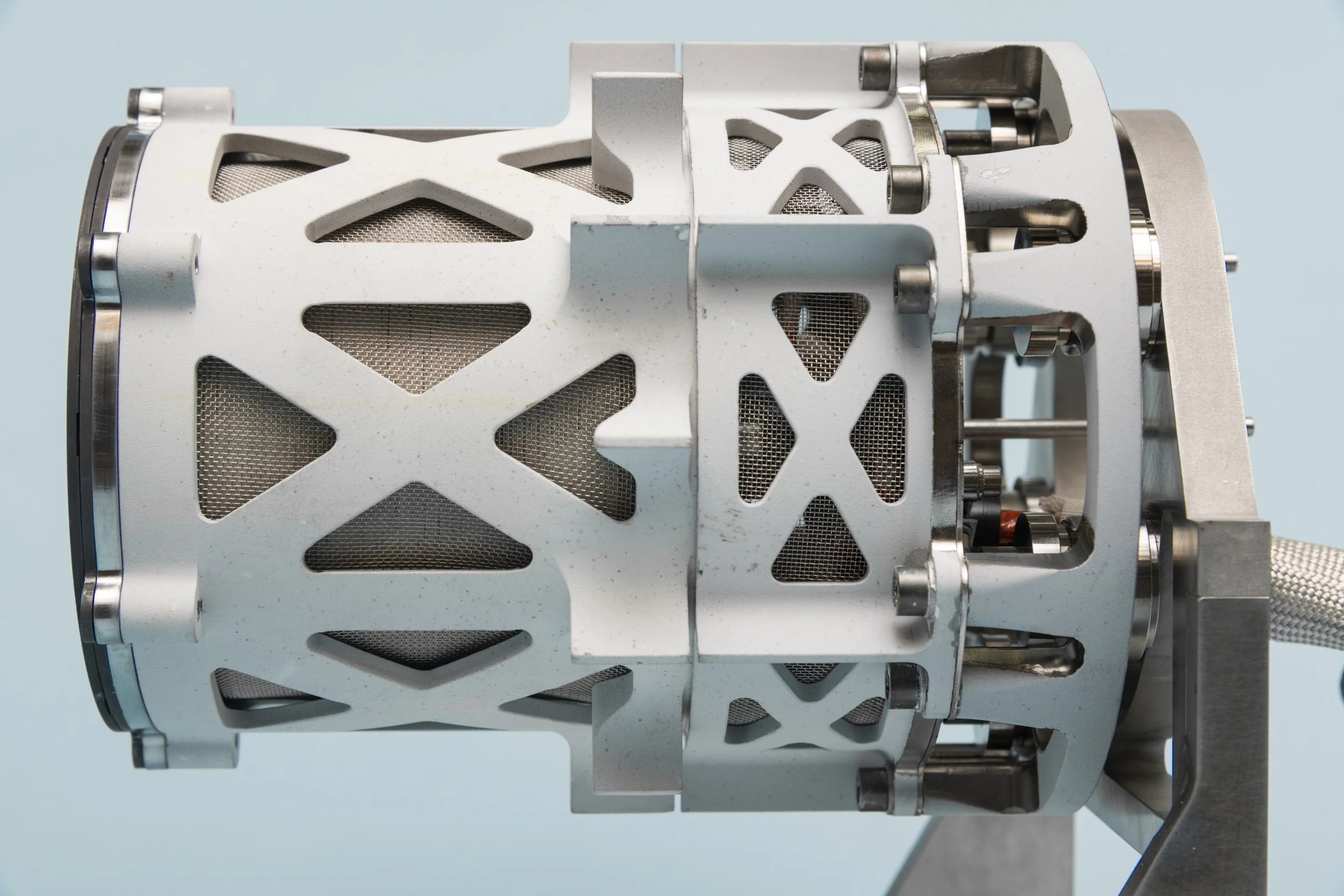 Close-up of a white mechanical or industrial device with metal components and mesh panels against a light blue background.