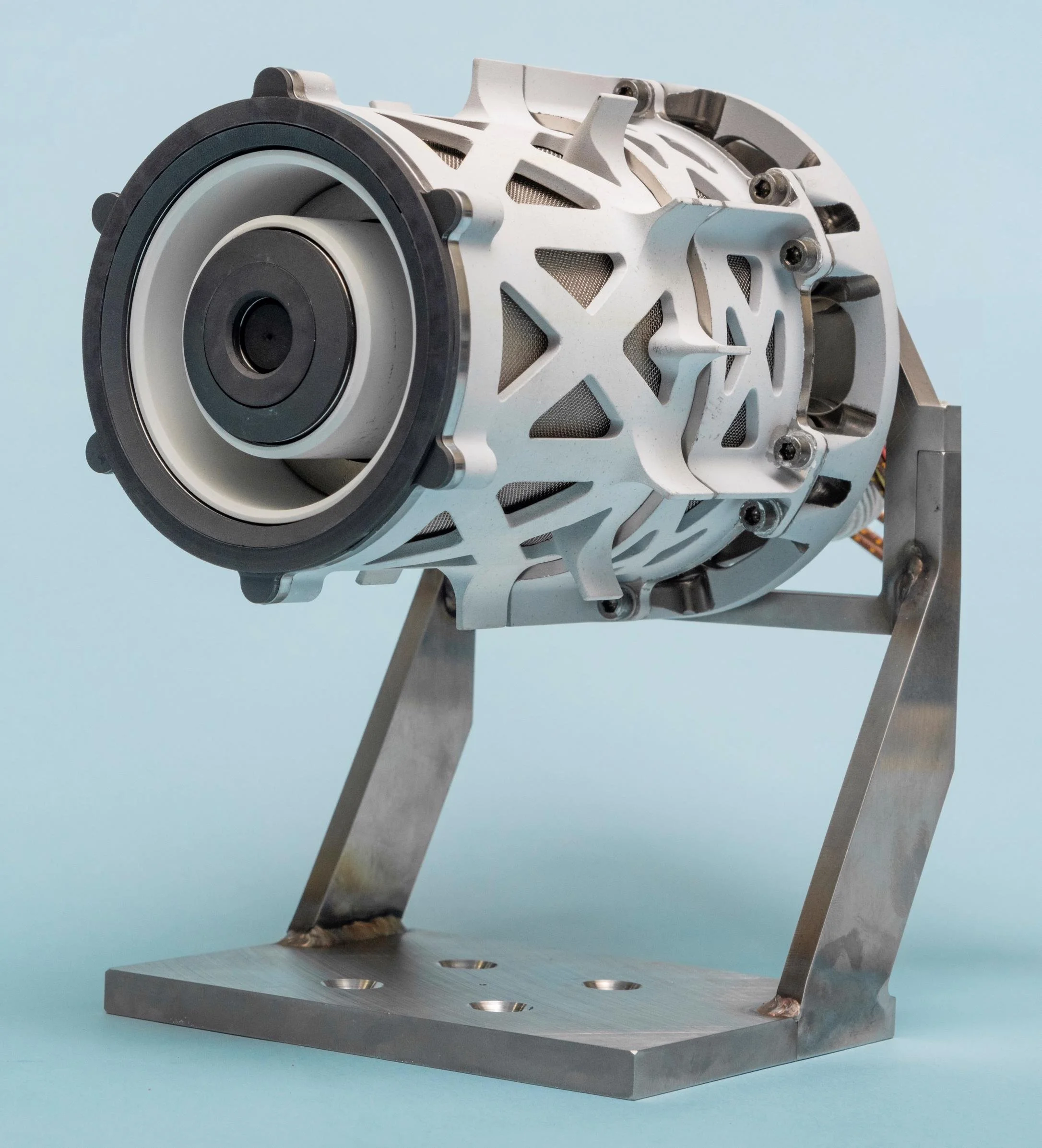 Metal mechanical part with circular component and structural frame mounted on a metal base, against a light blue background.