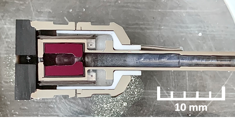 Close-up of a small electronic component with a metallic probe or needle inserted, showing internal parts and a 10 mm scale for size reference.