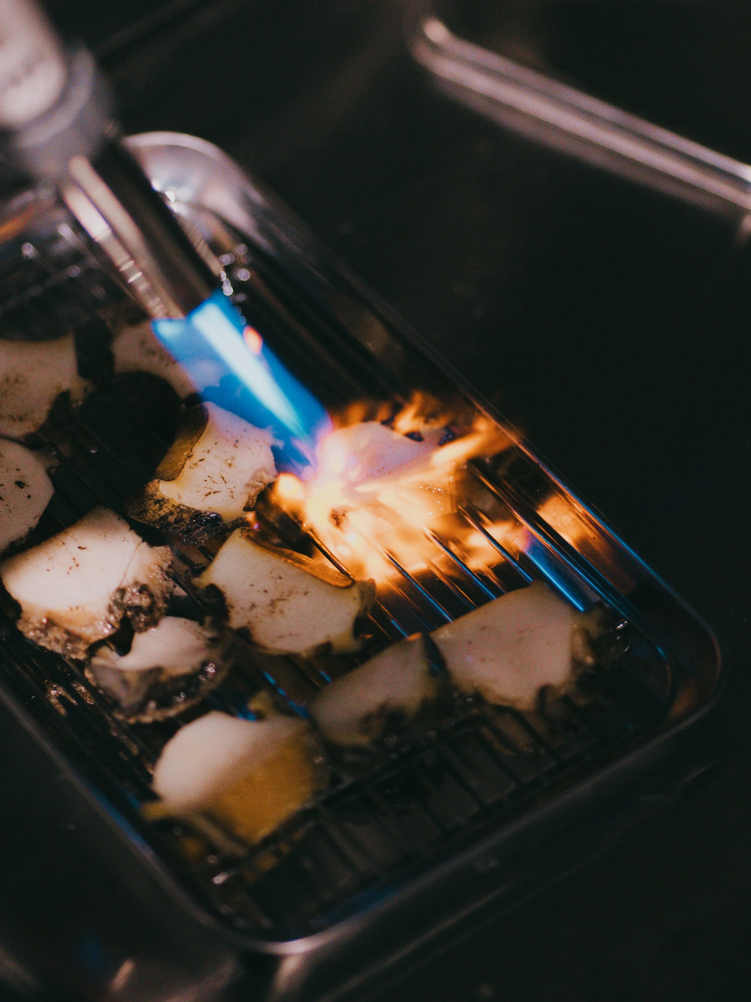 Pieces of cheese on a grill with blue flames from a blowtorch.