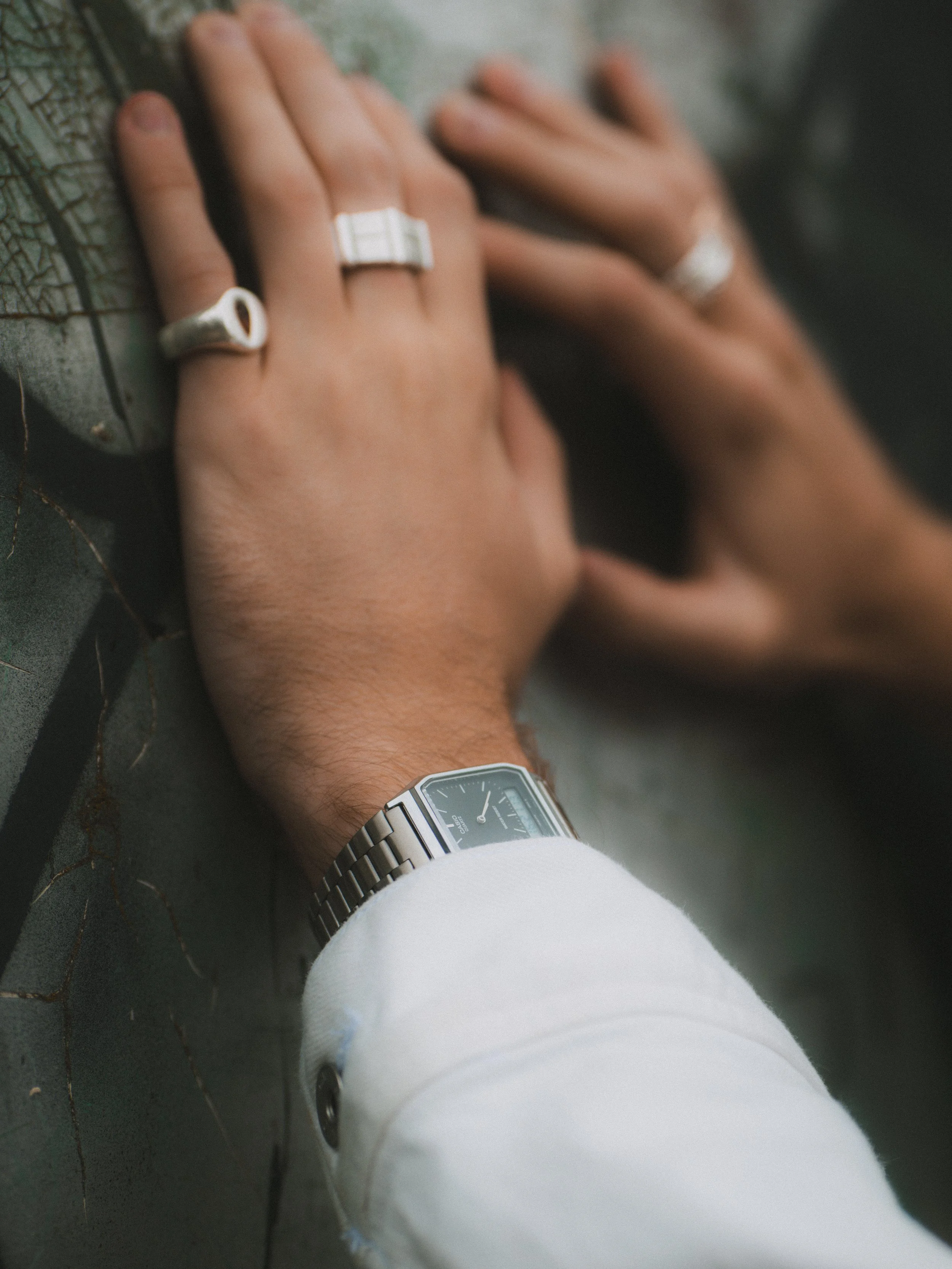 Close-up of a person's hand wearing rings and a bracelet, resting on a textured surface, with a silver watch on their wrist.