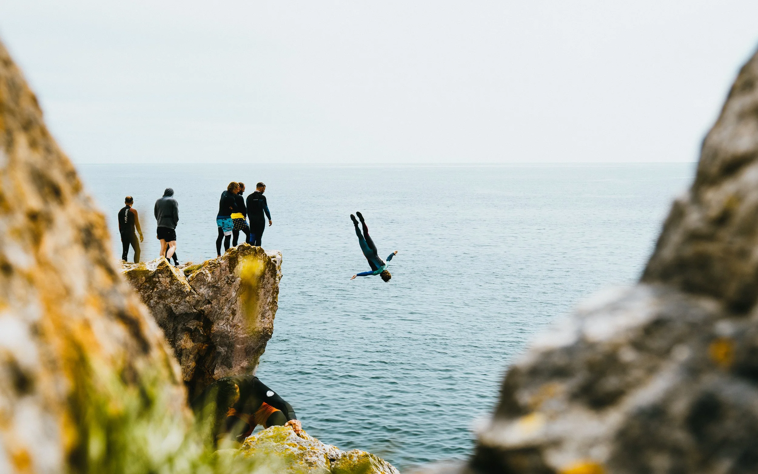 People standing on rocky cliff watching someone diving into the ocean.