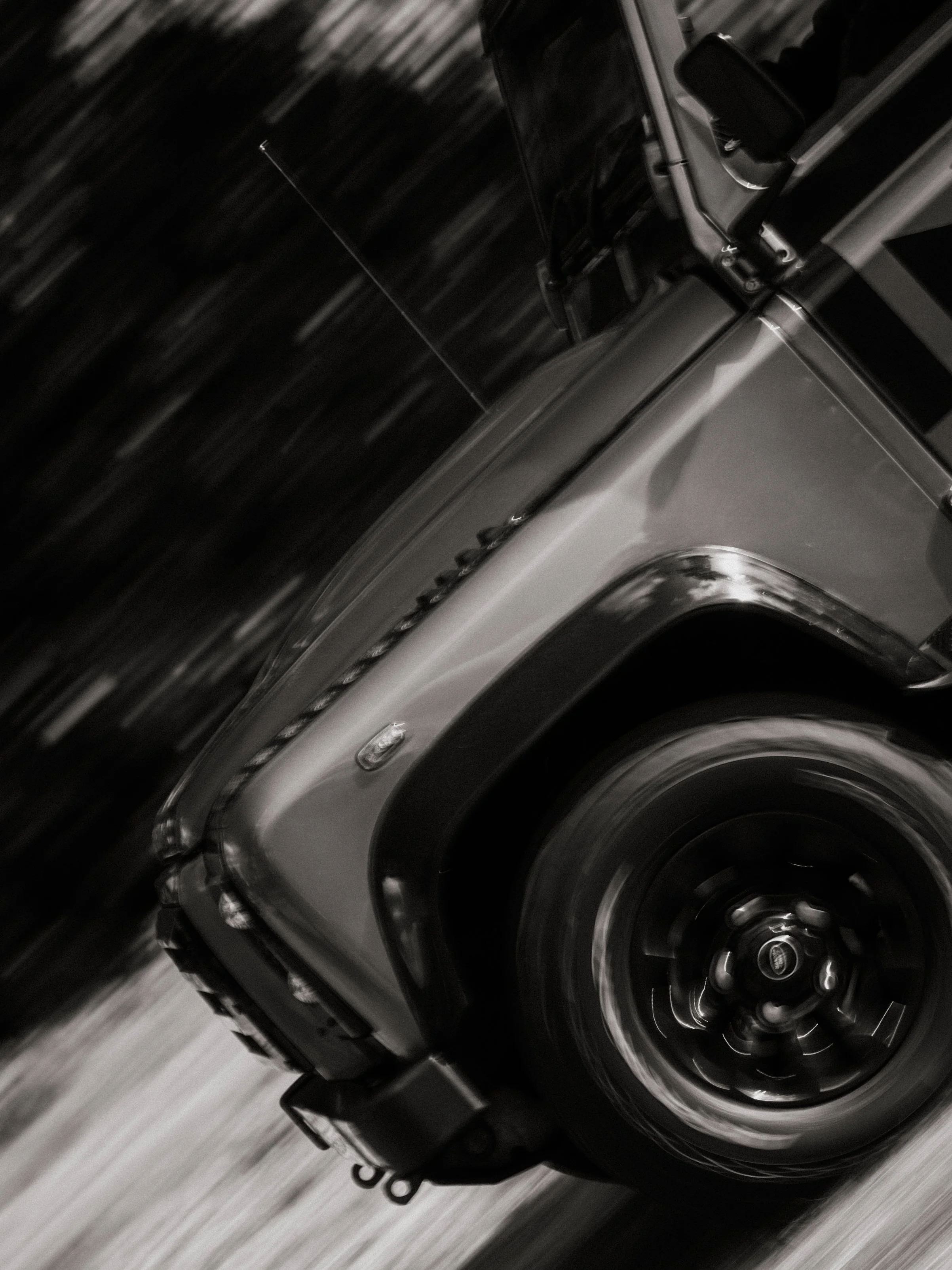 Close-up of a vintage car's front, showing the wheel, fender, and headlight in black and white.