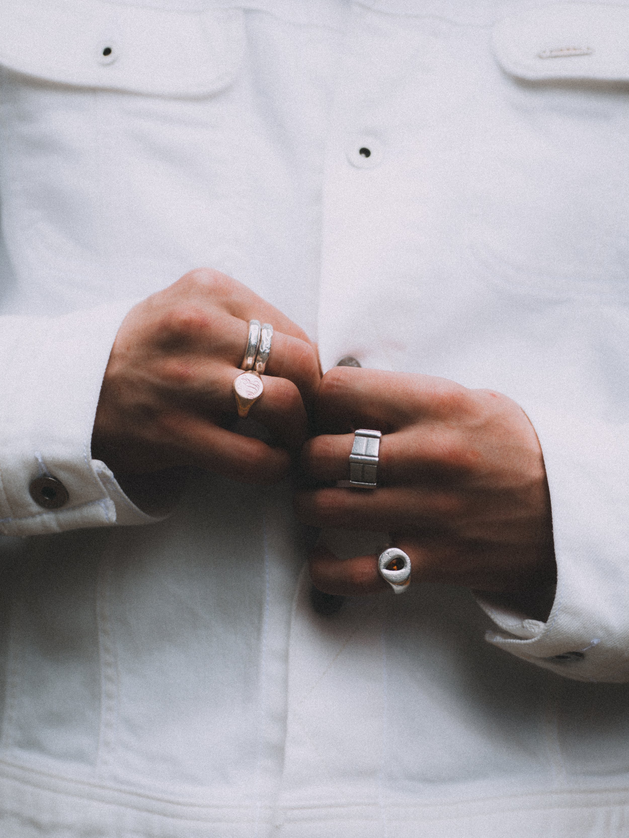 Close-up of a person wearing a white button-up shirt, adjusting their rings on their fingers.