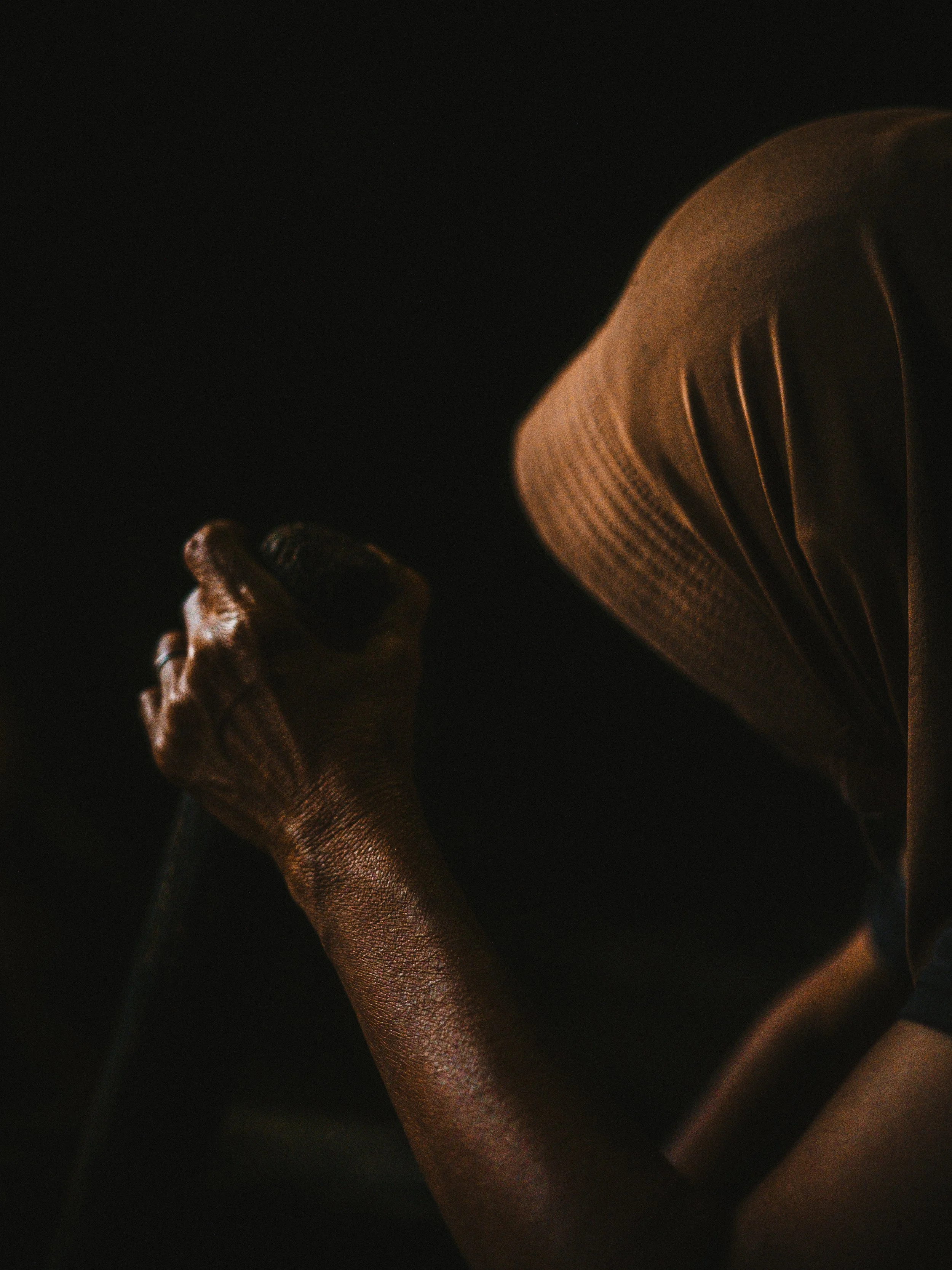 A person wearing a brown hoodie, holding a long object, with a dark background and low-key lighting.