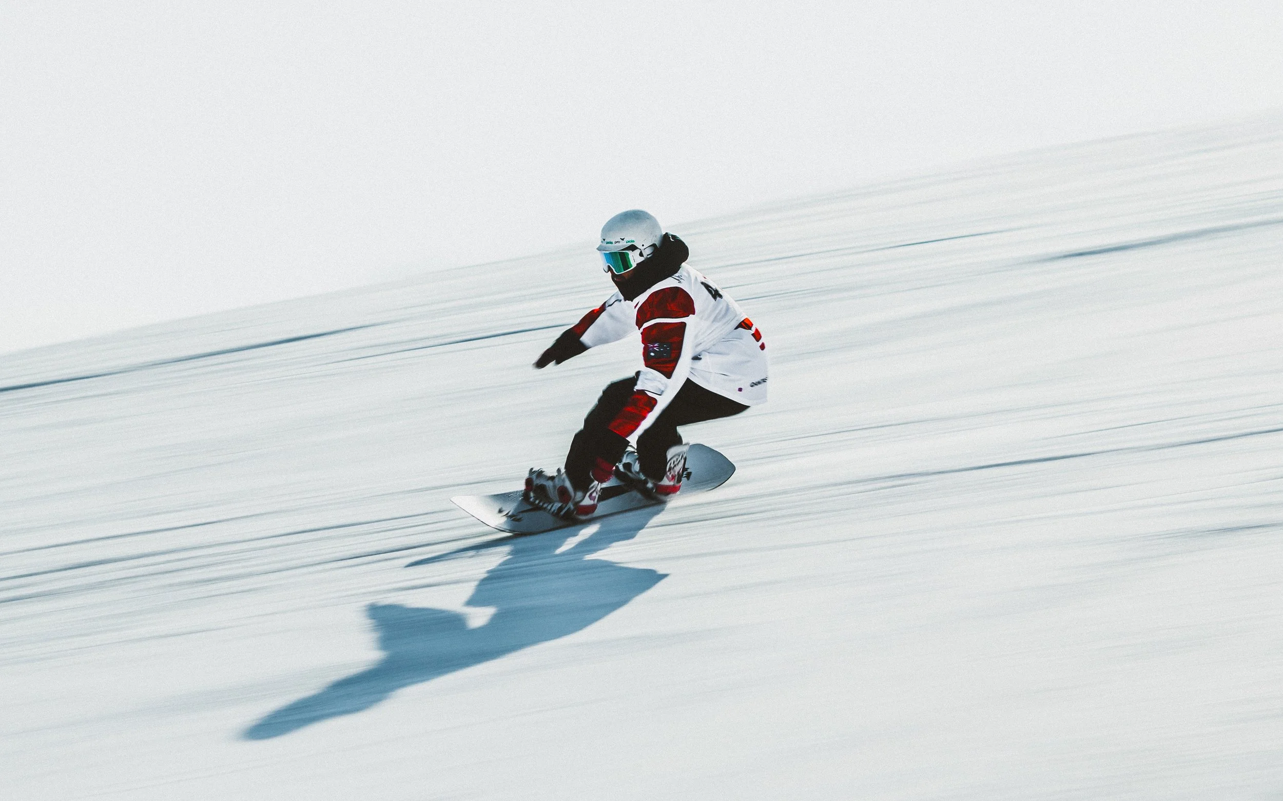 A skier in a white, red, and black ski suit and silver helmet snowboarding on a snowy slope.
