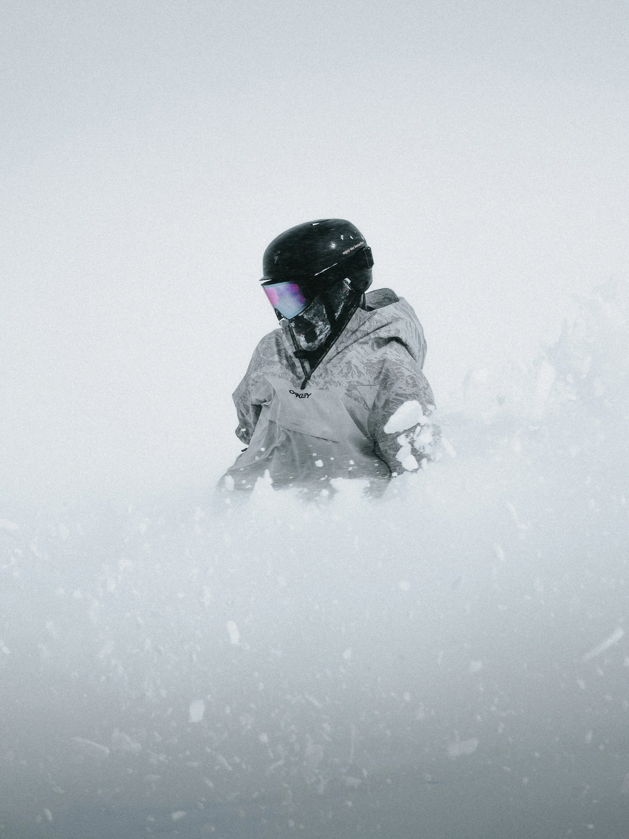 A person wearing a black helmet, ski goggles, and a gray winter jacket standing in a snowy landscape.