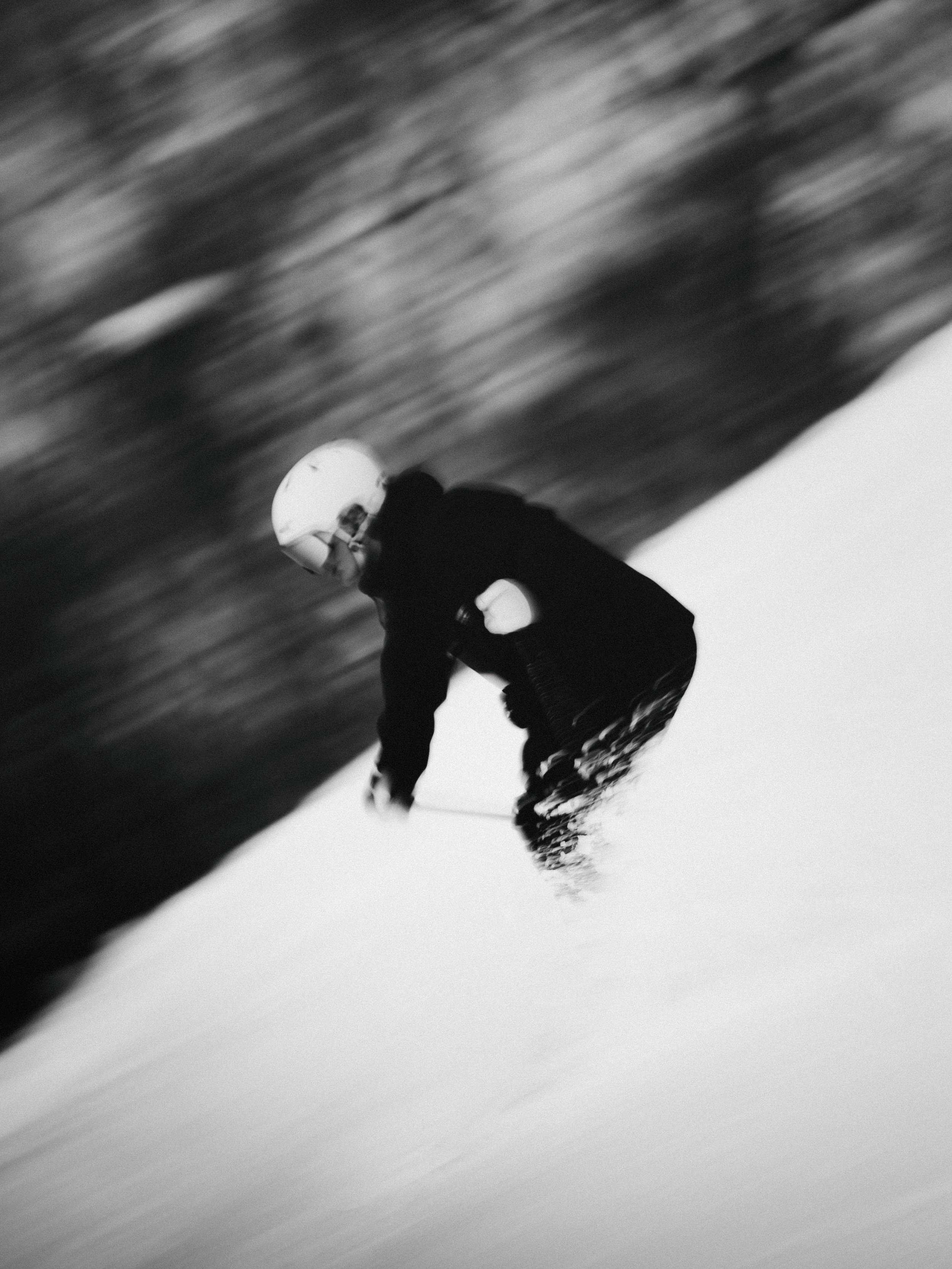A person skiing down a snow-covered slope, wearing a helmet, in black and white.