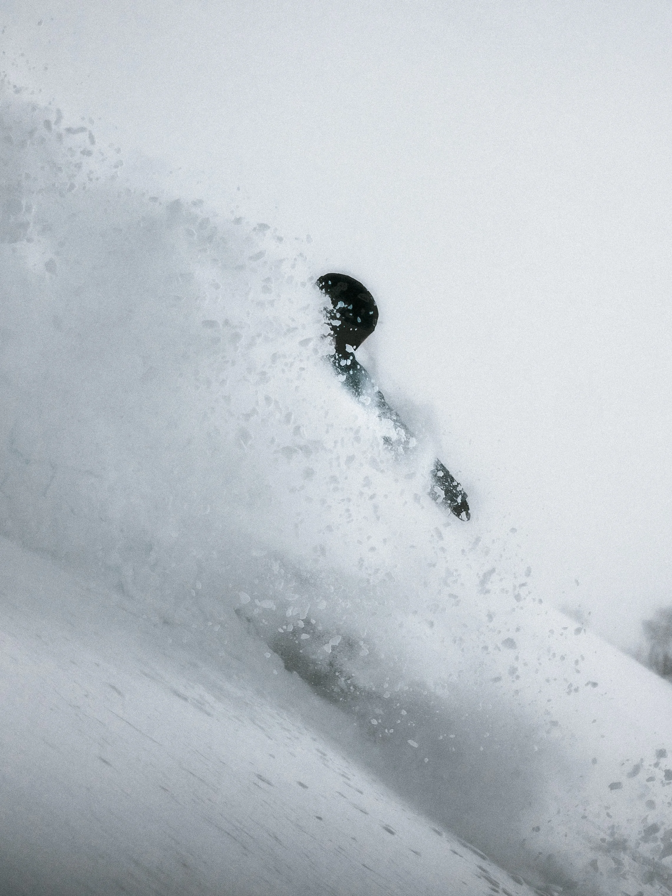 A skier on a snowy slope carving through fresh powder, creating a spray of snow in the air.